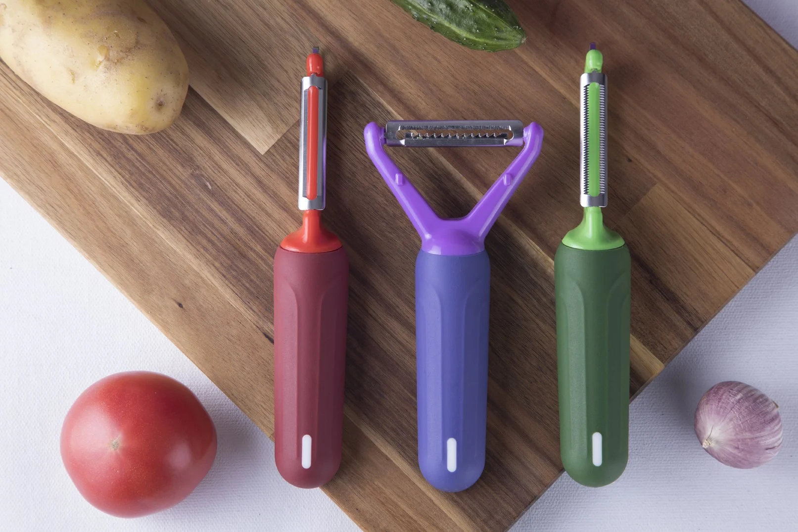 Three Cookduo Food Prep Steelcore peelers in red, purple Y-peeler, and green, with internal metal reinforcement for a slim, rigid profile