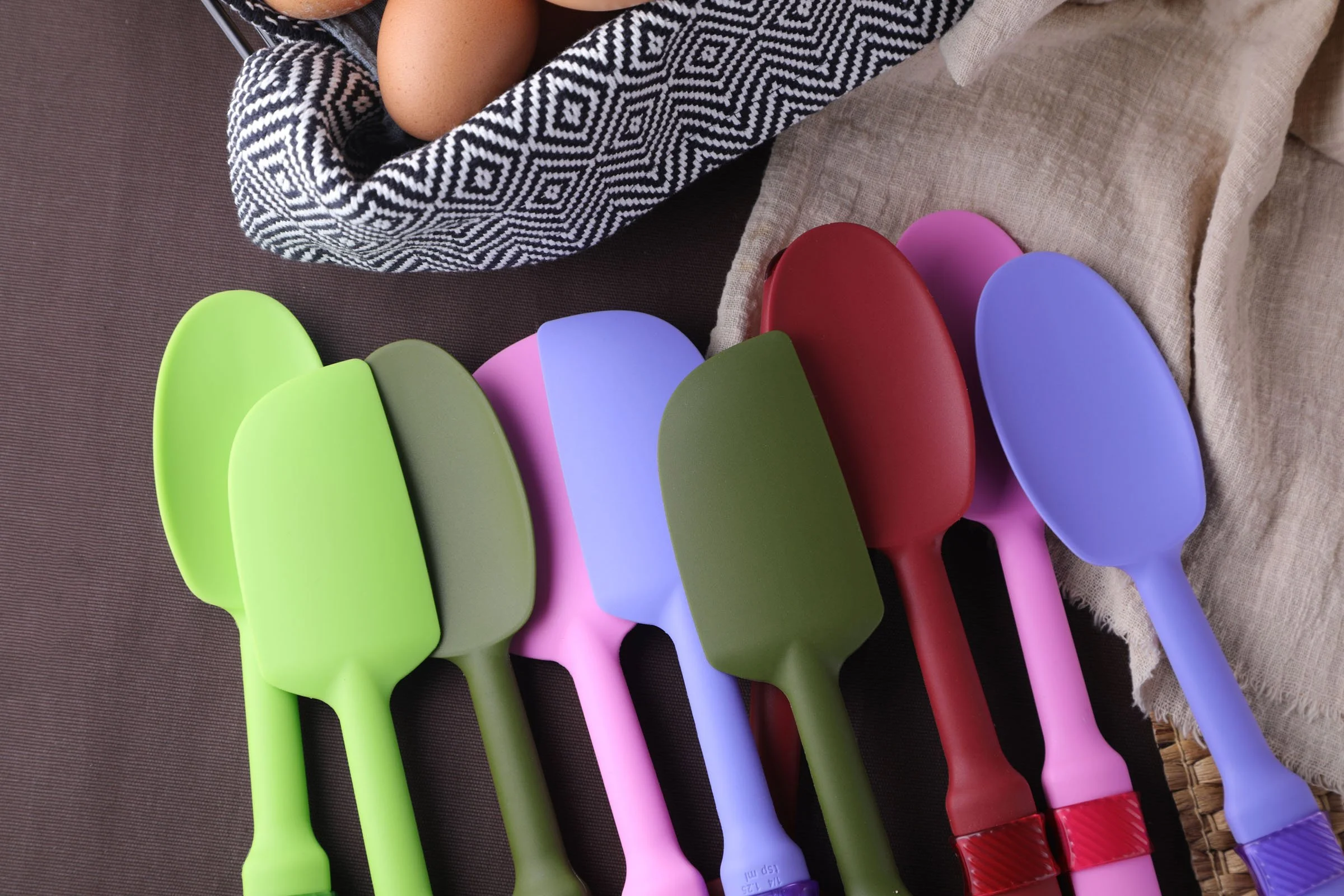 Cookduo Mix and Measure silicone spoons and spatulas in five colorways, showing the two-in-one design with measuring spoon integrated into each handle