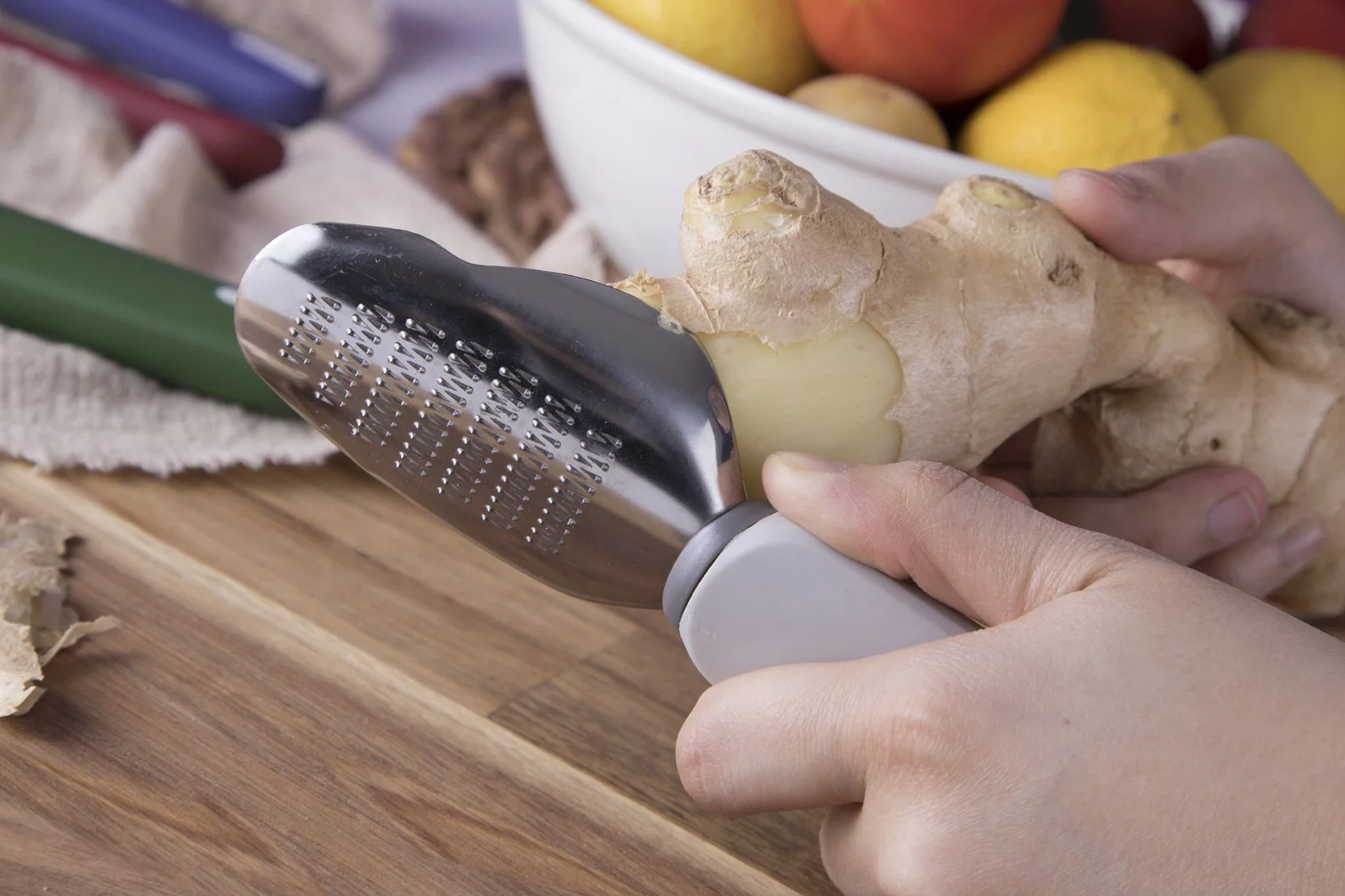 Hands grating fresh ginger root with the Cookduo Food Prep ginger tool, showing the stainless steel grating surface and ergonomic handle