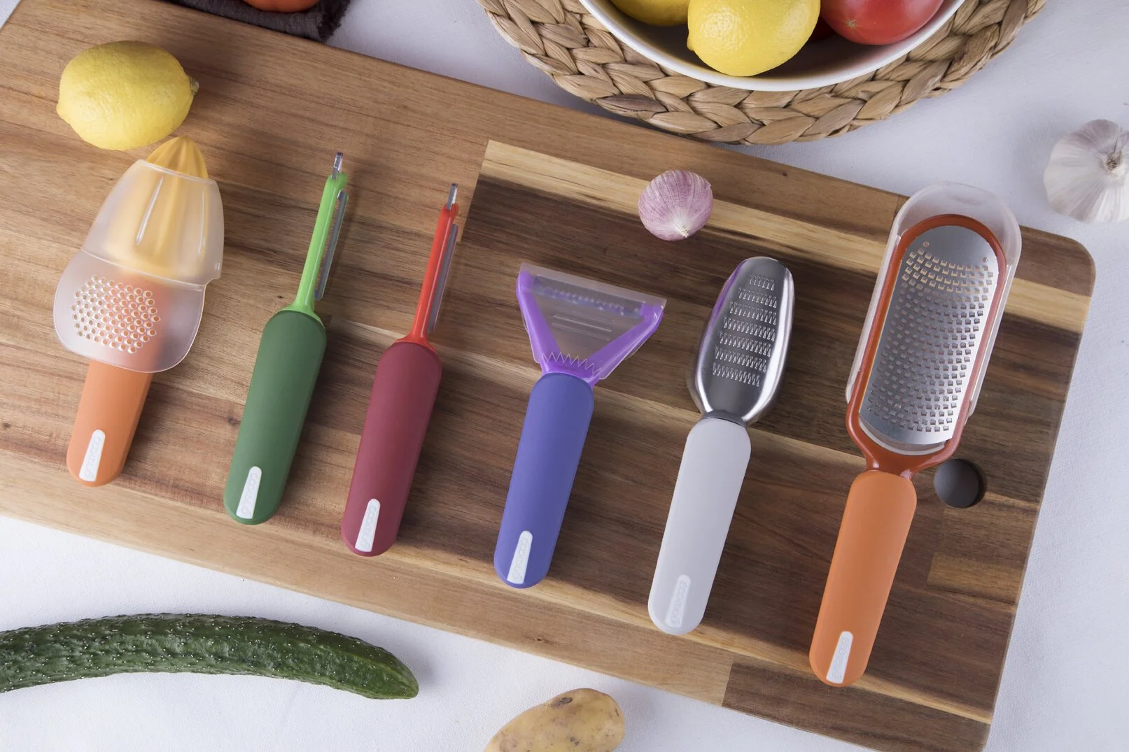 Cookduo Food Prep Line kitchen tool collection top-down on a cutting board with produce, including the lemon reamer, peelers, ginger grater, and zester