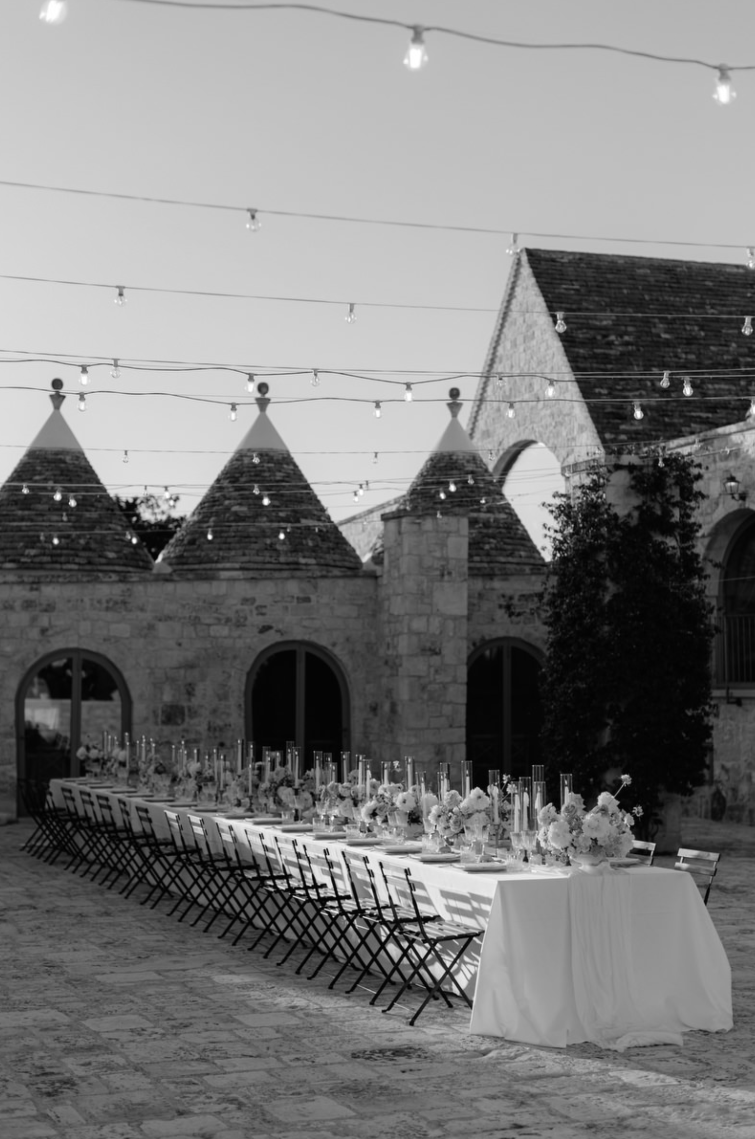 Black and white wedding photo at a Puglian masseria with traditional trulli structures in the background.