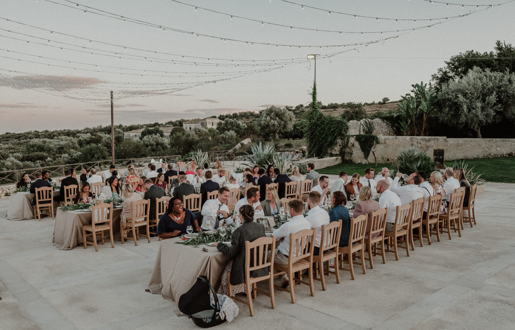 Long wedding reception tables set outdoors at evening at a historic Baroque estate in the Monti Iblei, southeastern Sicily.