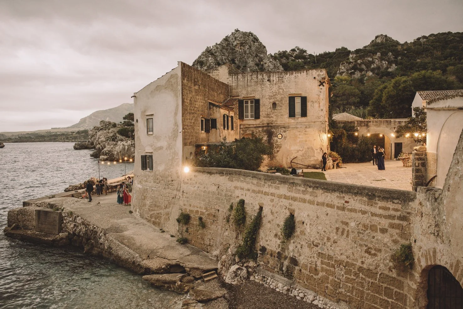 Tonnara di Scopello illuminated with fairy lights at dusk, creating an atmospheric evening setting for a Sicilian wedding.