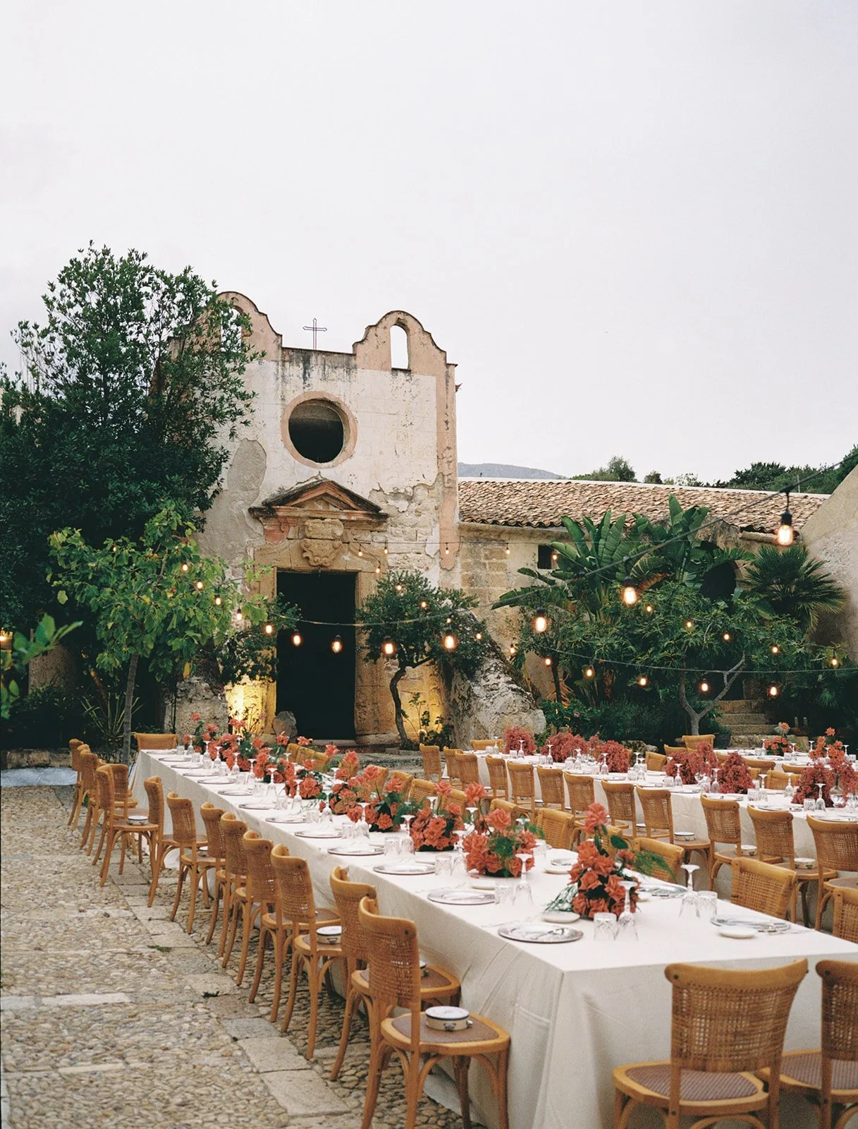Long wedding reception tables set in the historic stone courtyard at Tonnara di Scopello, Sicily.