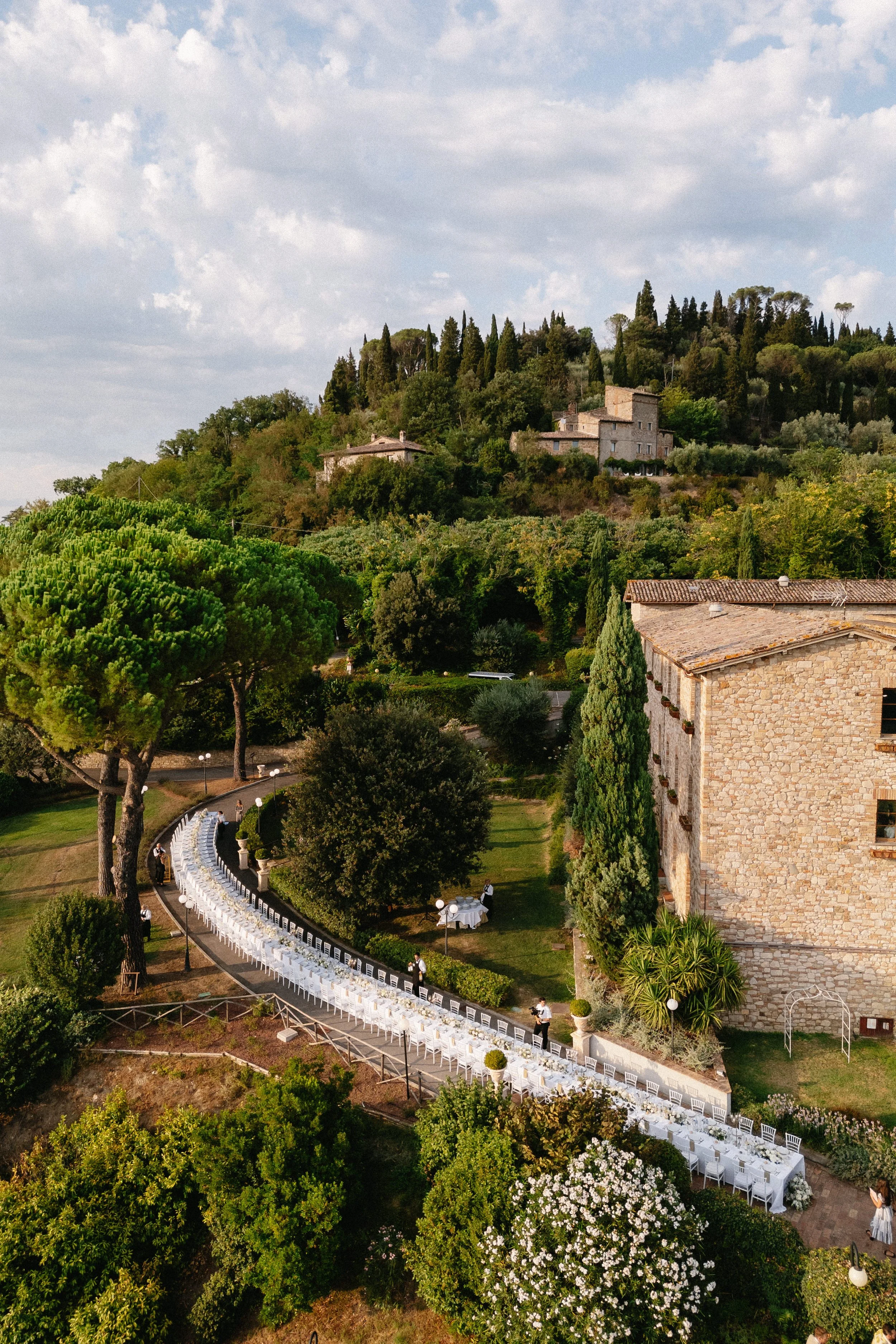 Long wedding reception table curving along a garden path at a 12th-century monastery in Umbria, Italy.