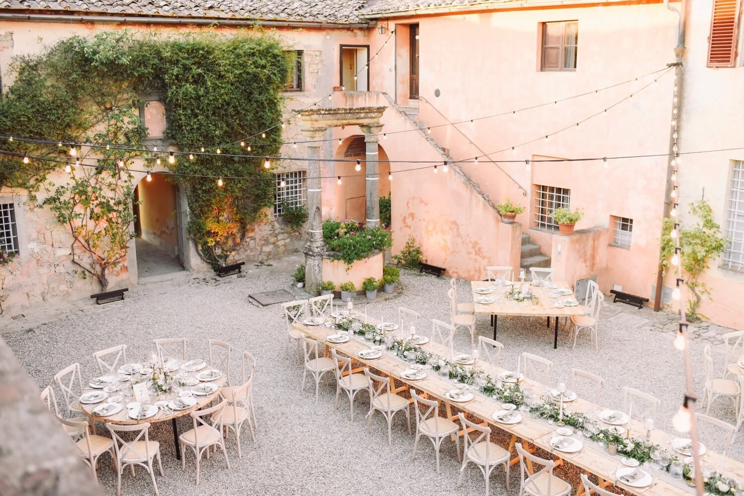 Wedding dinner set in a courtyard with fairy lights at a 16th-century wine-producing estate near Siena, Tuscany.