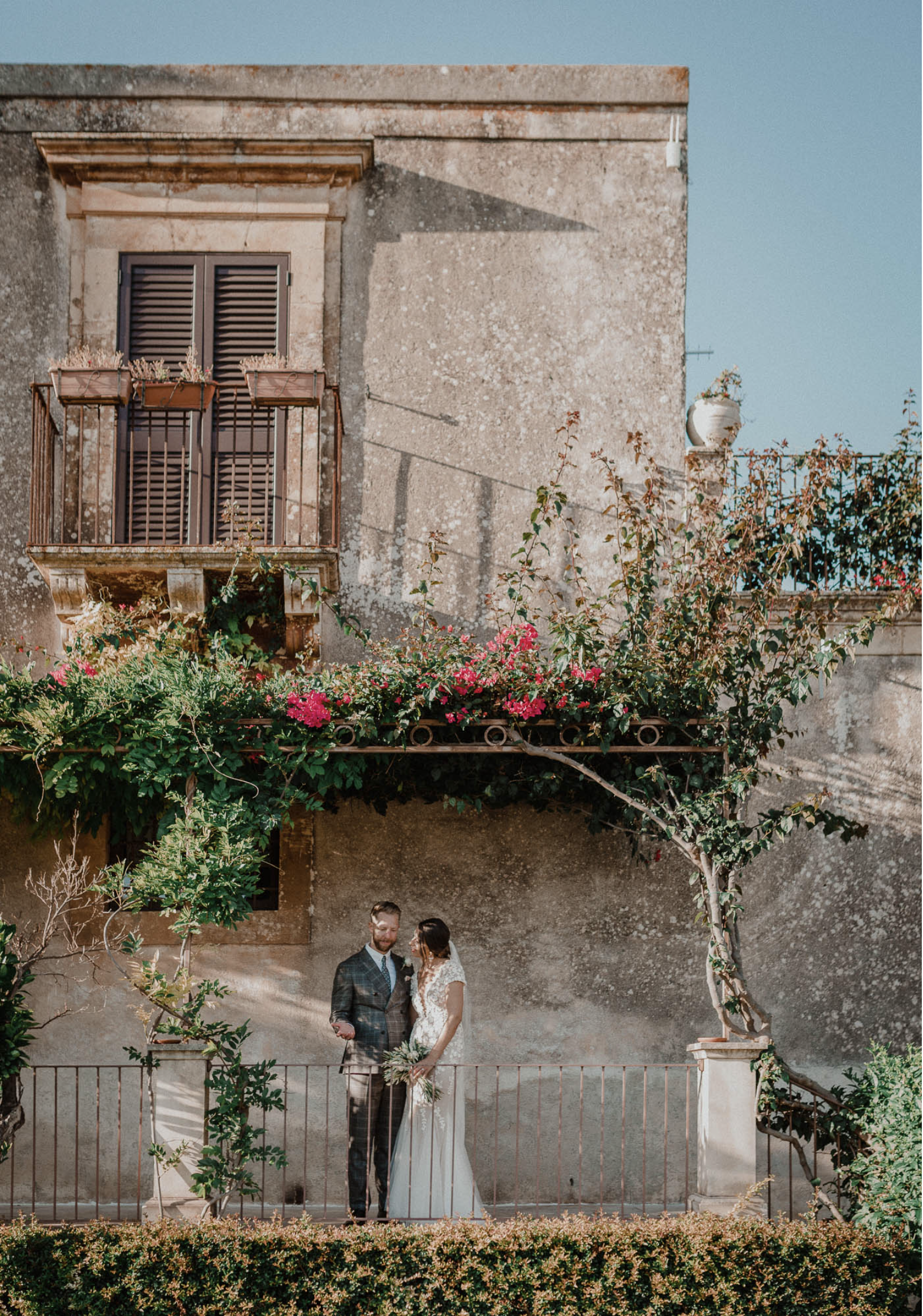 Couple standing beside a stone wall covered in climbing plants at a restored rural wedding venue in southeastern Sicily.
