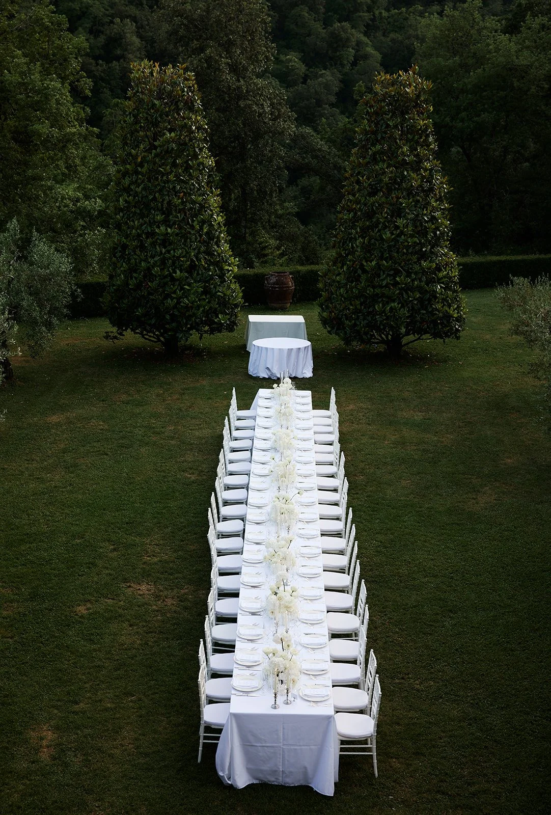 Long alfresco dining table with simple white floral and silver decor at intimate Tuscan wedding at Villa Catureglio