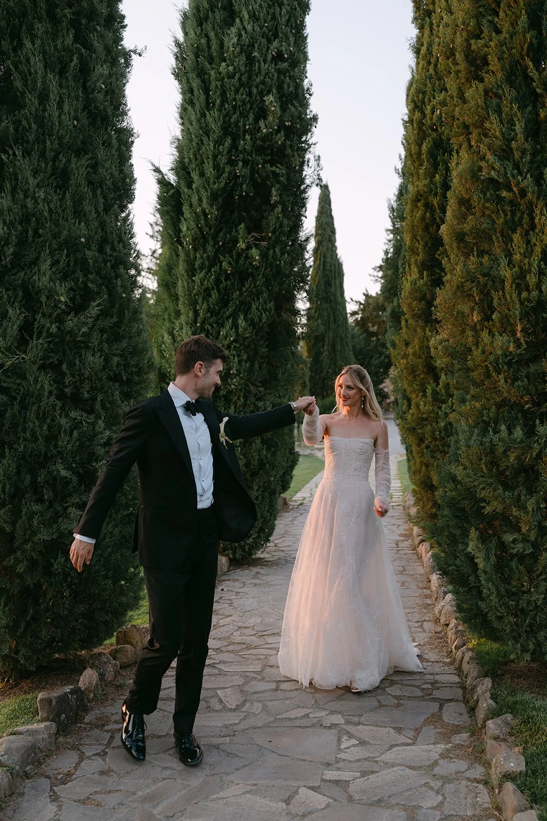 Couple strolling through an avenue of trees at Borgo Laticastelli, a medieval monastery wedding venue in Umbria, Italy.