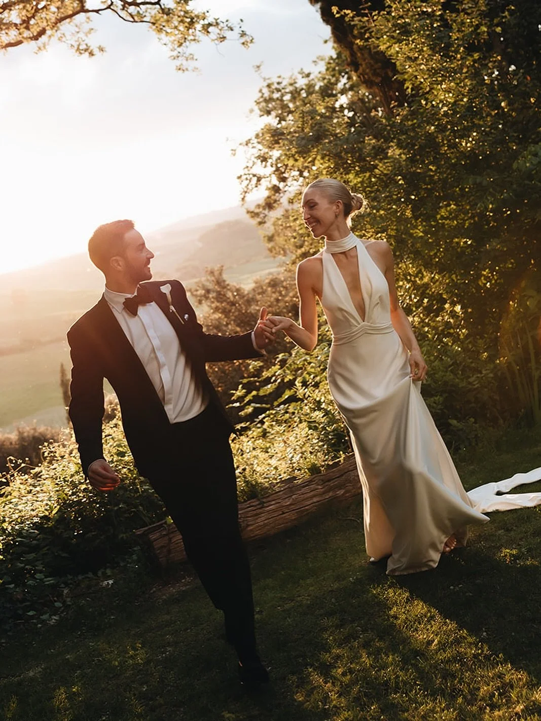 Couple walking along a hilltop terrace at golden hour above the Crete Senesi hills, Tuscany.