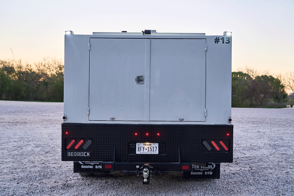 People unloading equipment from a black utility vehicle and a trailer, with outdoor trees and a clear blue sky in the background.