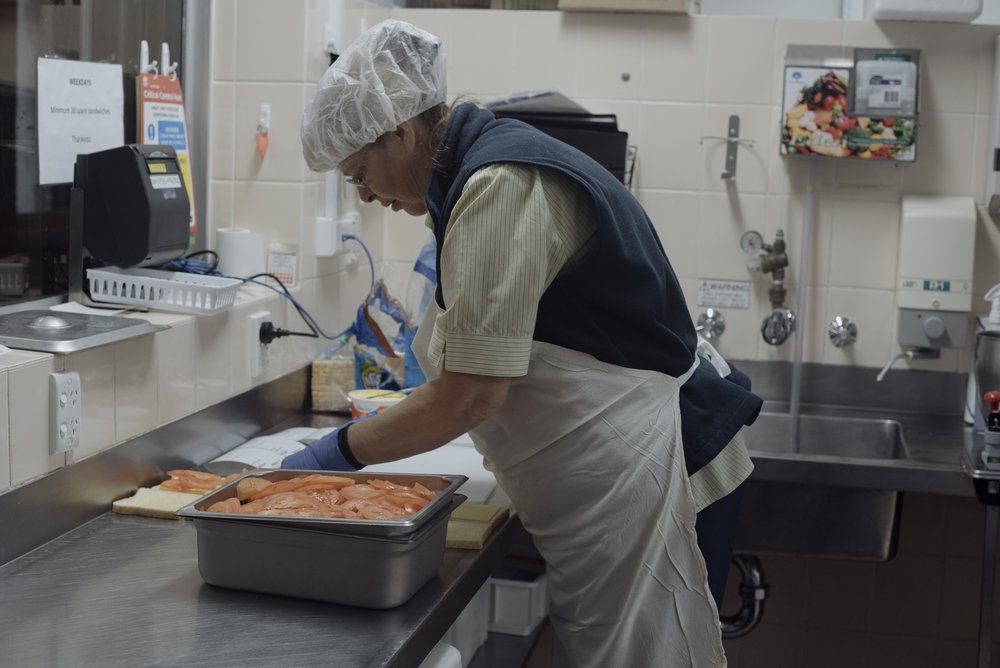  Margaret Baker preparing food. The staff used to work together in an assembly to prepare the food service. By 2021 new systems meant that they work more individually. 