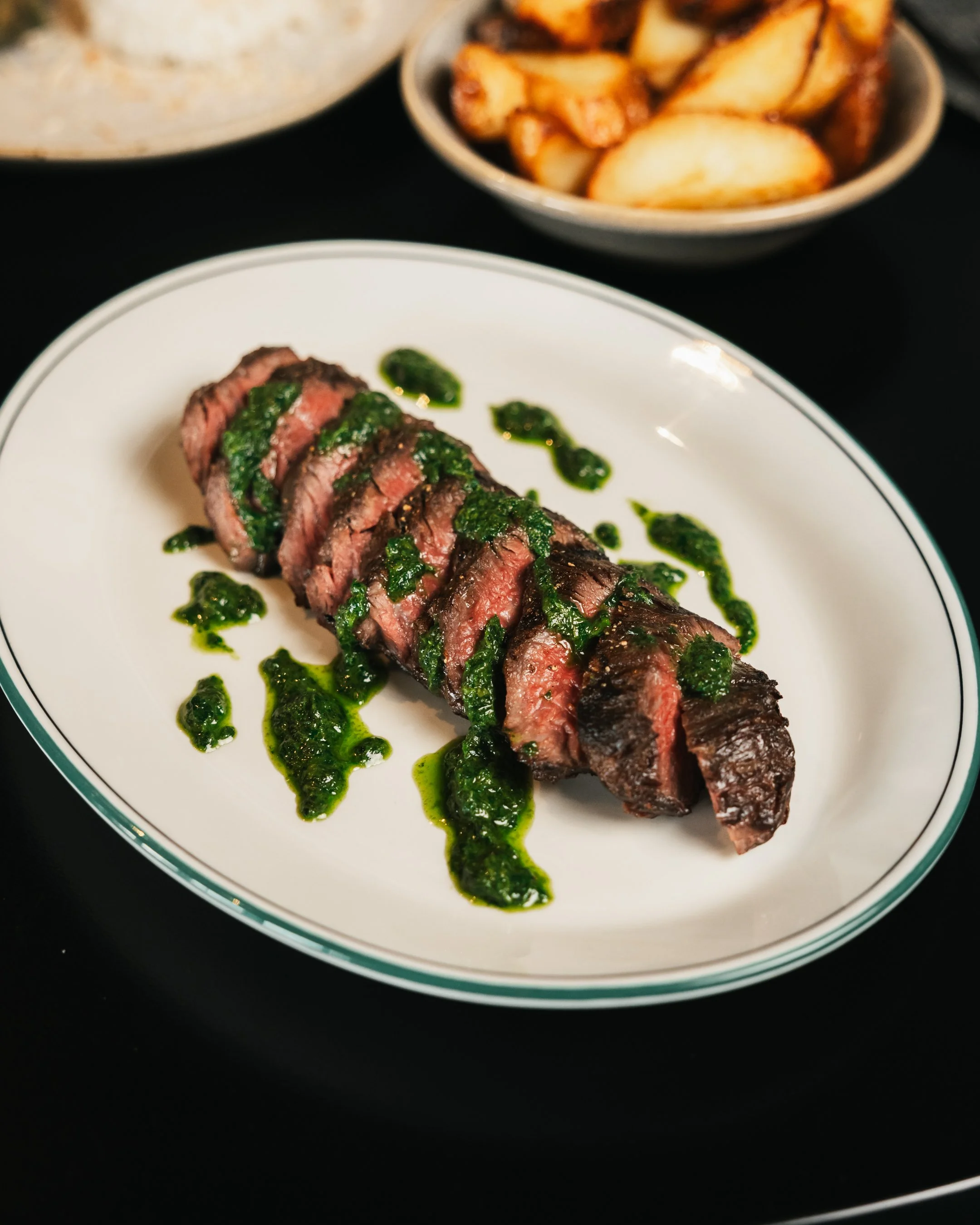A black plate of sliced medium-rare steak topped with green onions, red onions, garlic, and a dark sauce, labeled 'Wednesday Steak' at the top.