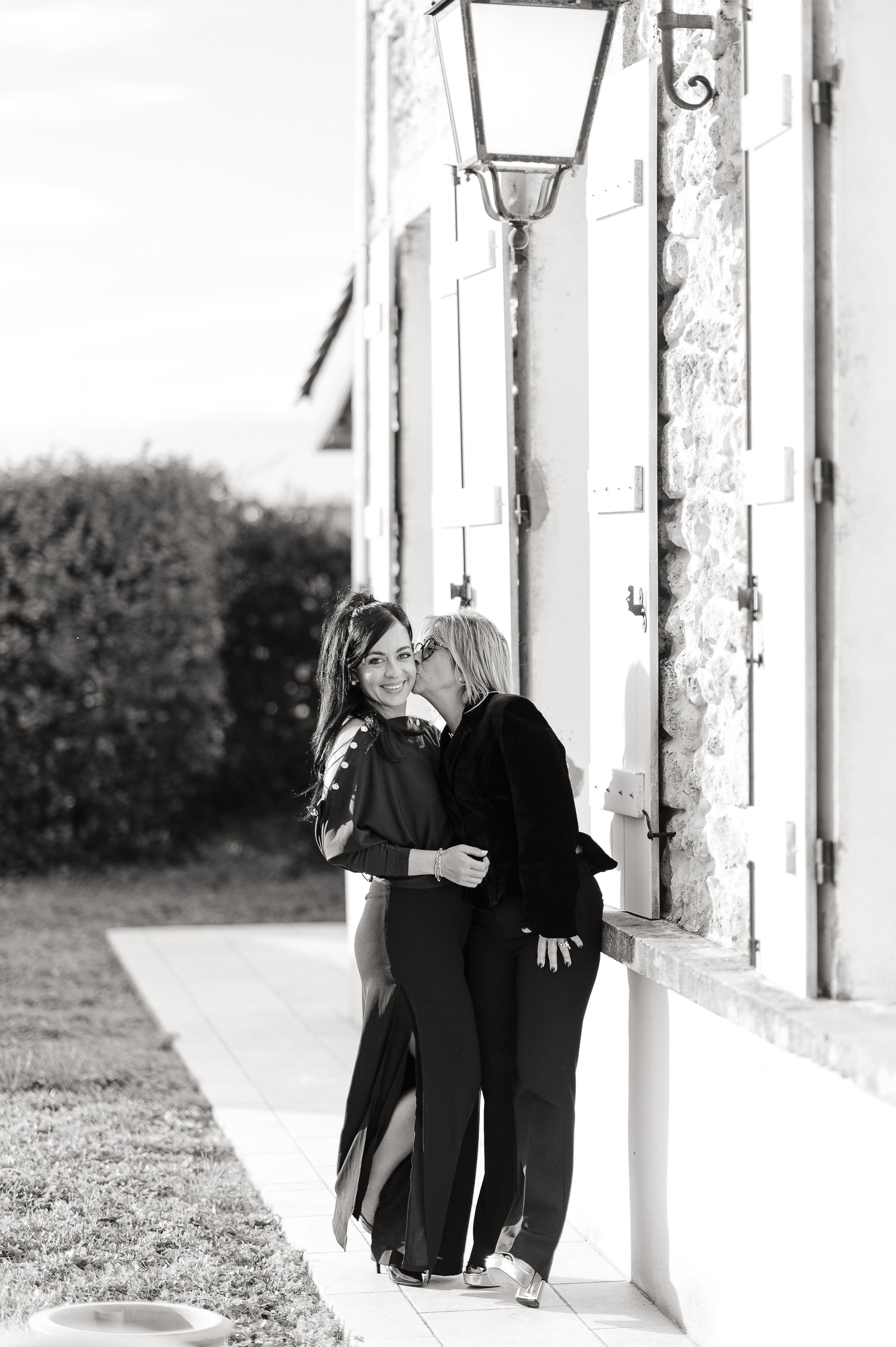 Séance photo famille à Bordeaux en noir et blanc avec deux femmes adultes partageant un moment complice devant la maison familiale