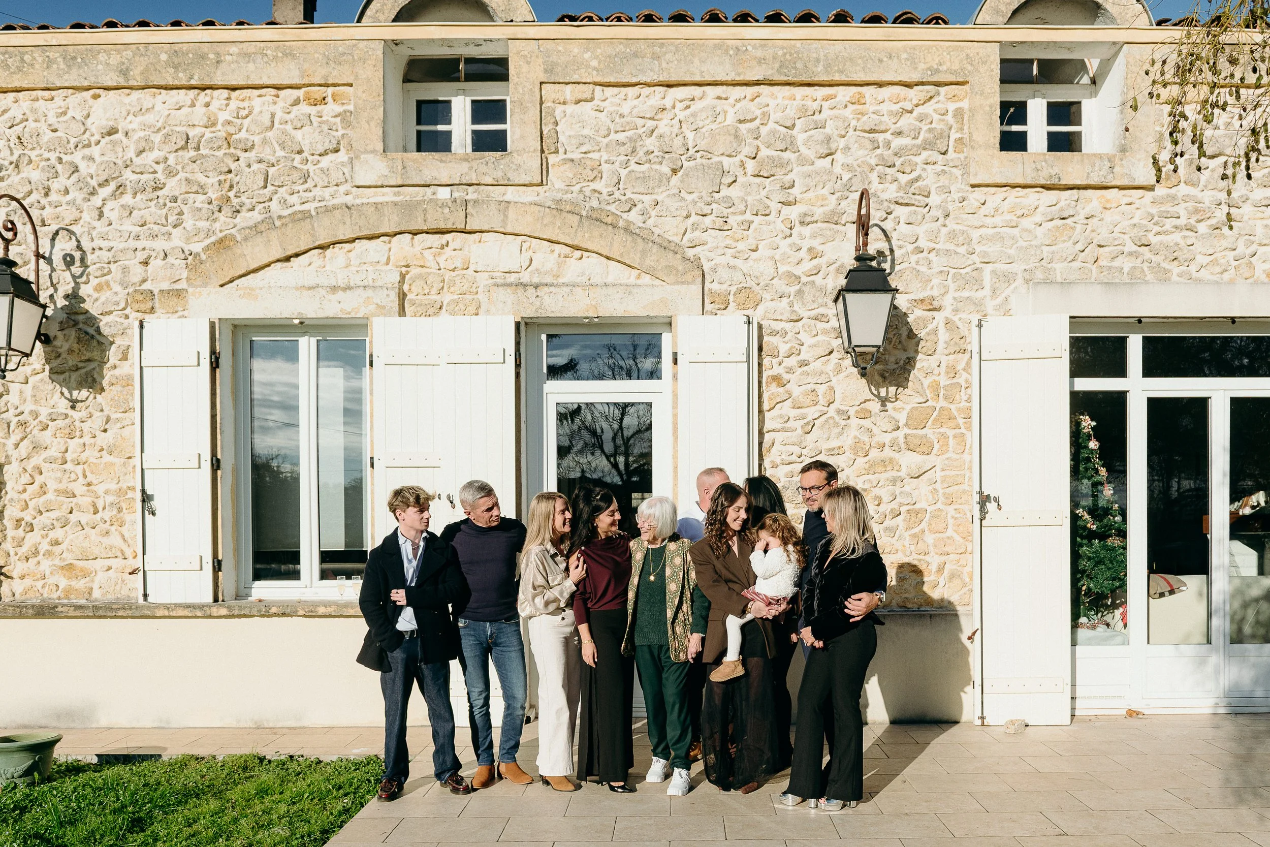 Photographe famille à Bordeaux capturant un groupe familial multi-générationnel devant la maison de famille