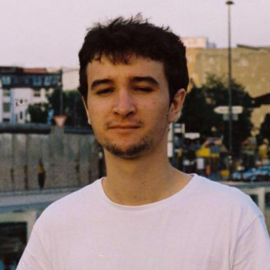 A person in a white shirt stands outdoors in an urban setting.