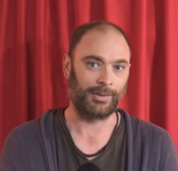 Man with beard in front of red curtain
