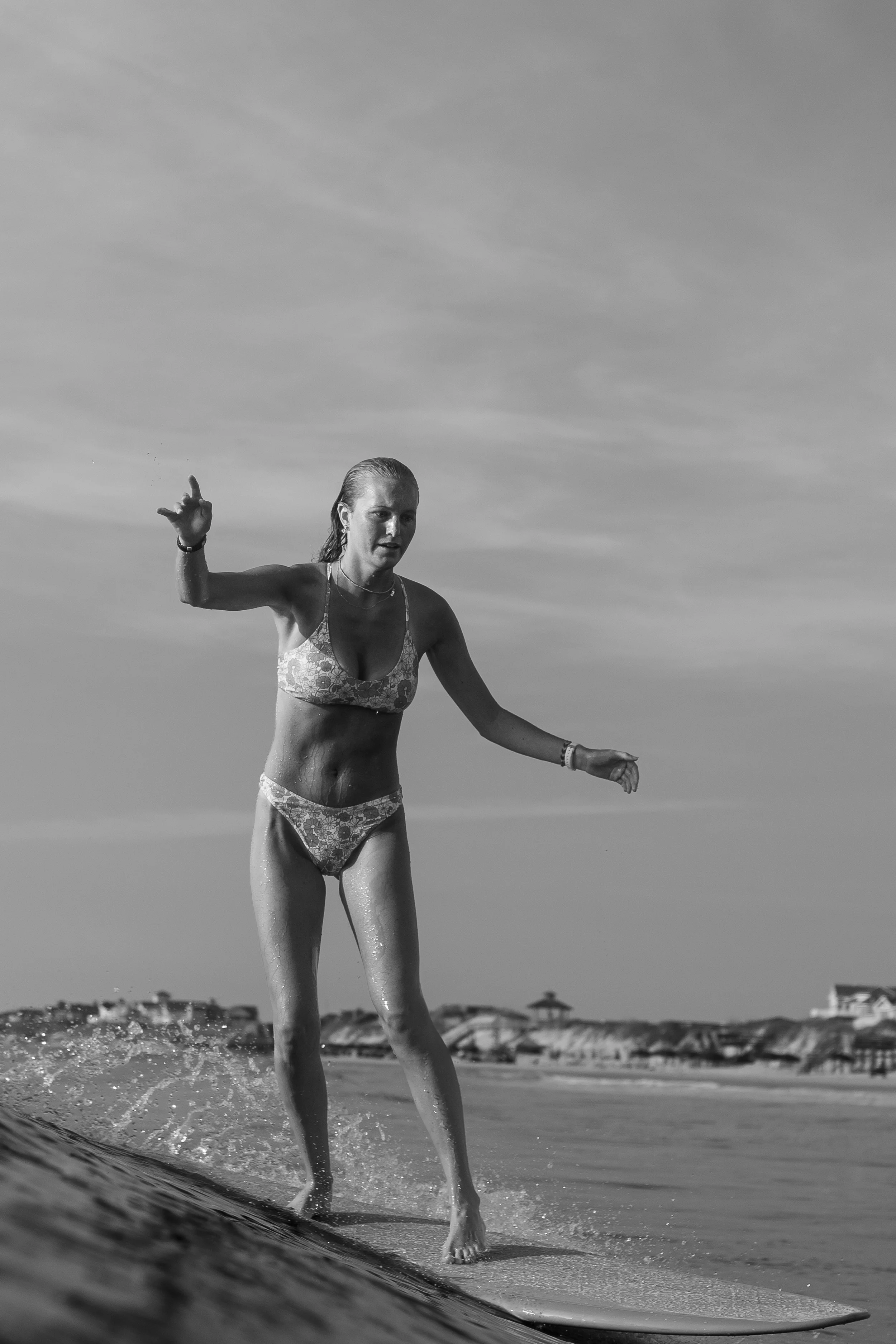A woman in a bikini walking on the beach with water splashing around her legs, under a cloudy sky.