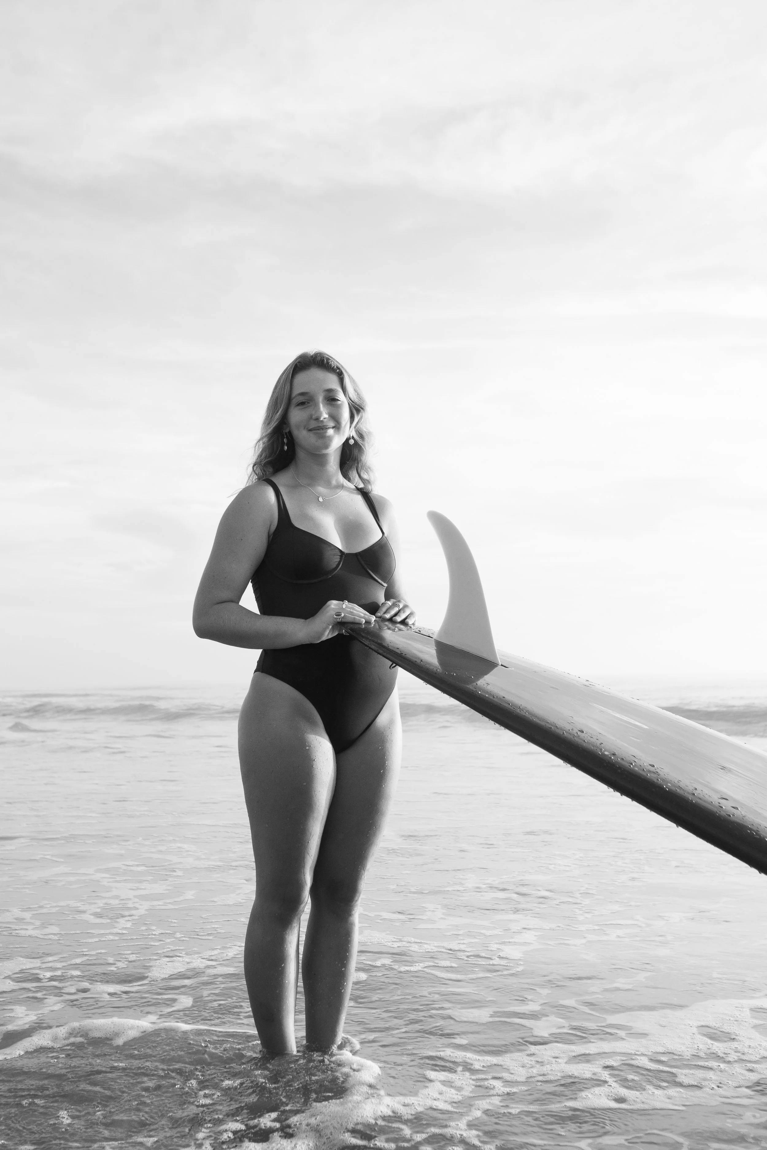 A woman in a swimsuit standing in the ocean holding a surfboard.
