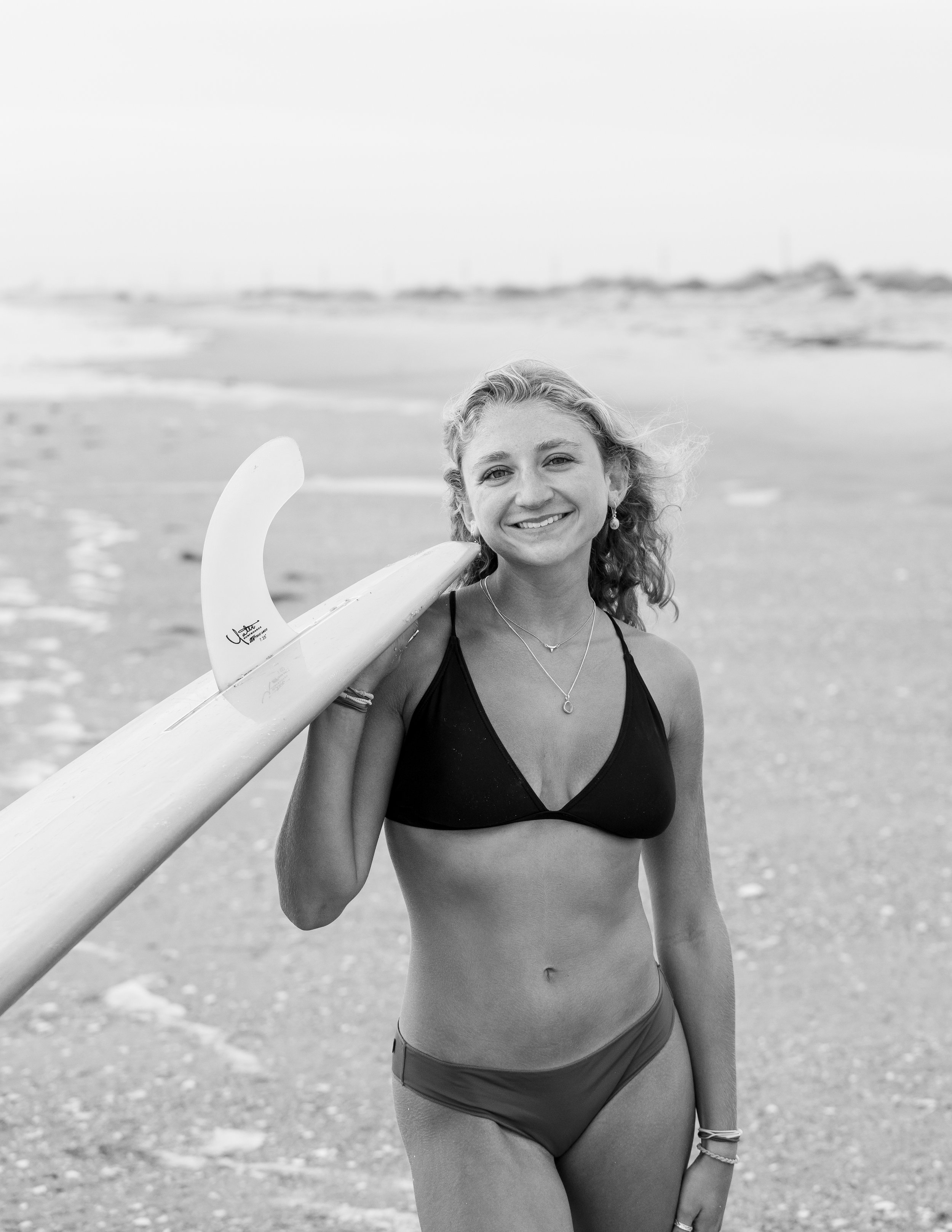 Smiling woman in a bikini holding a surfboard on the beach.