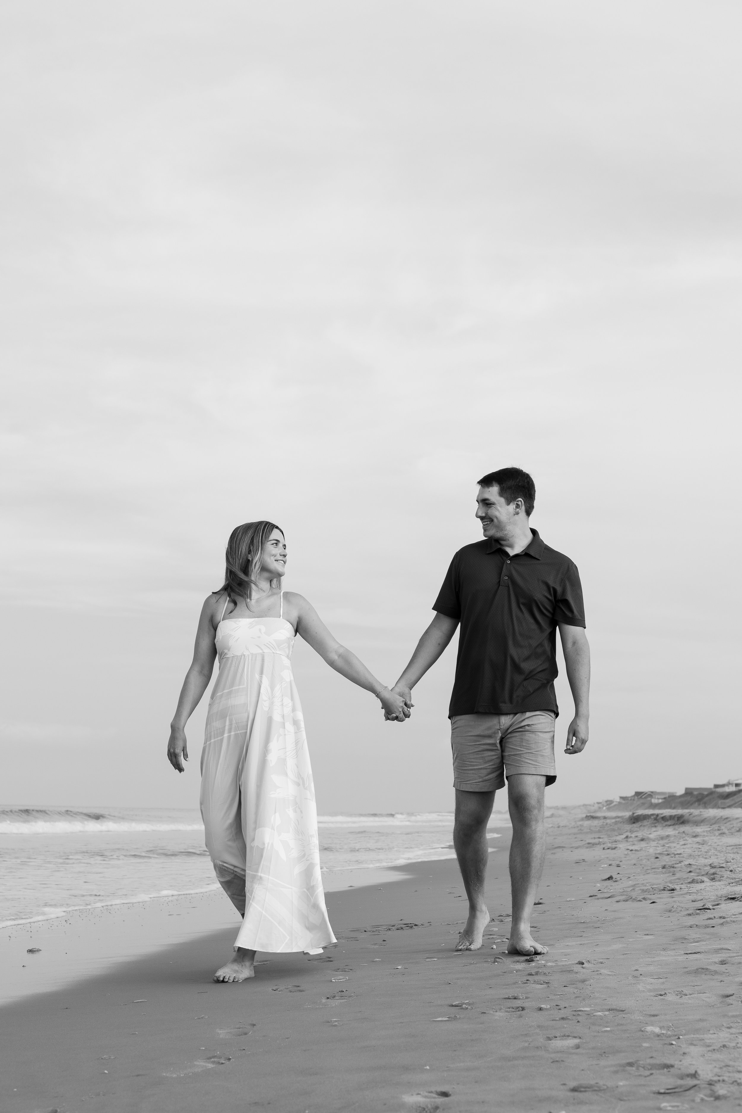 A smiling man and woman holding hands and walking on the beach.