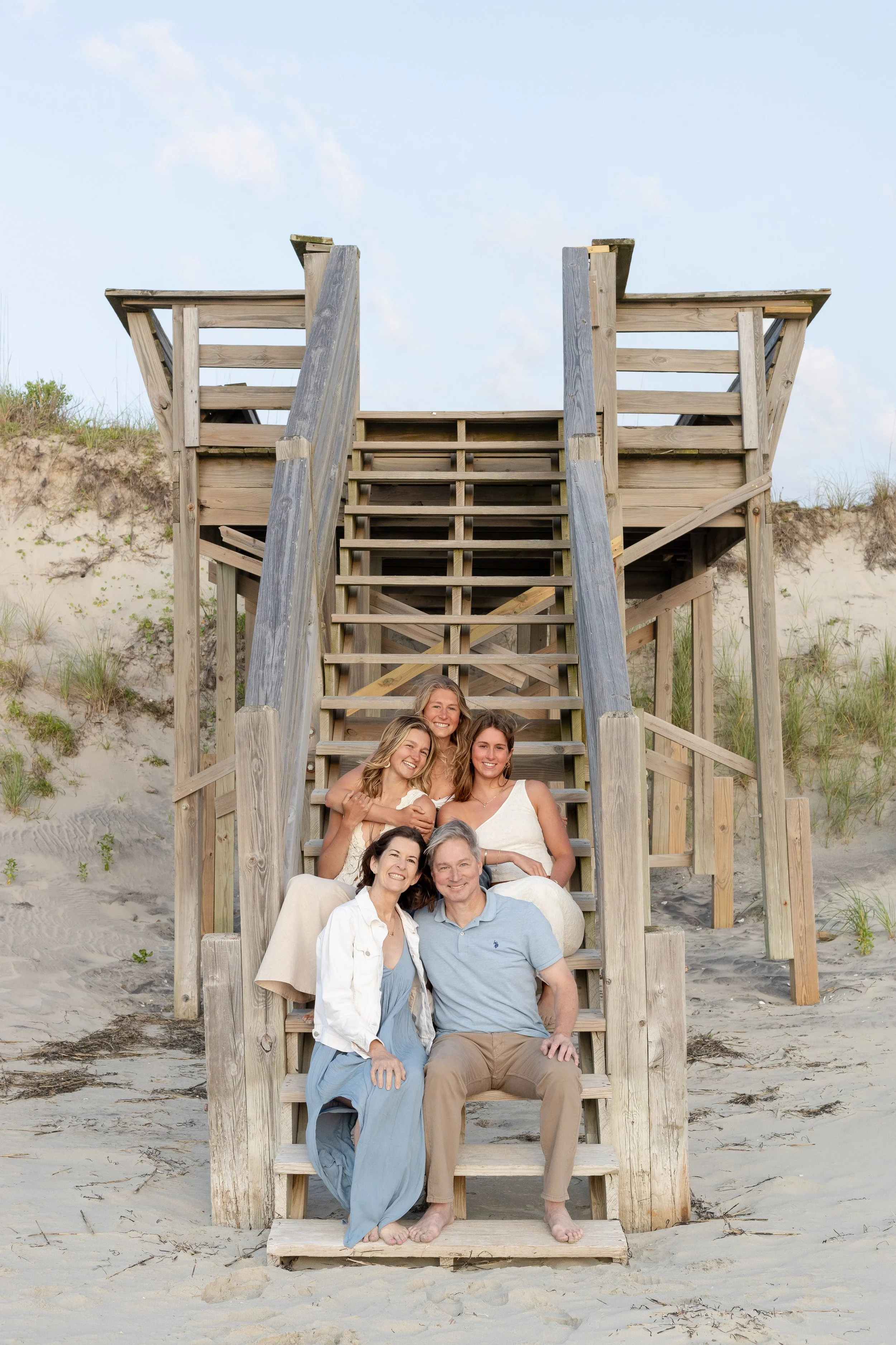 Group of six people sitting on a wooden lifeguard tower on the beach, smiling at the camera.