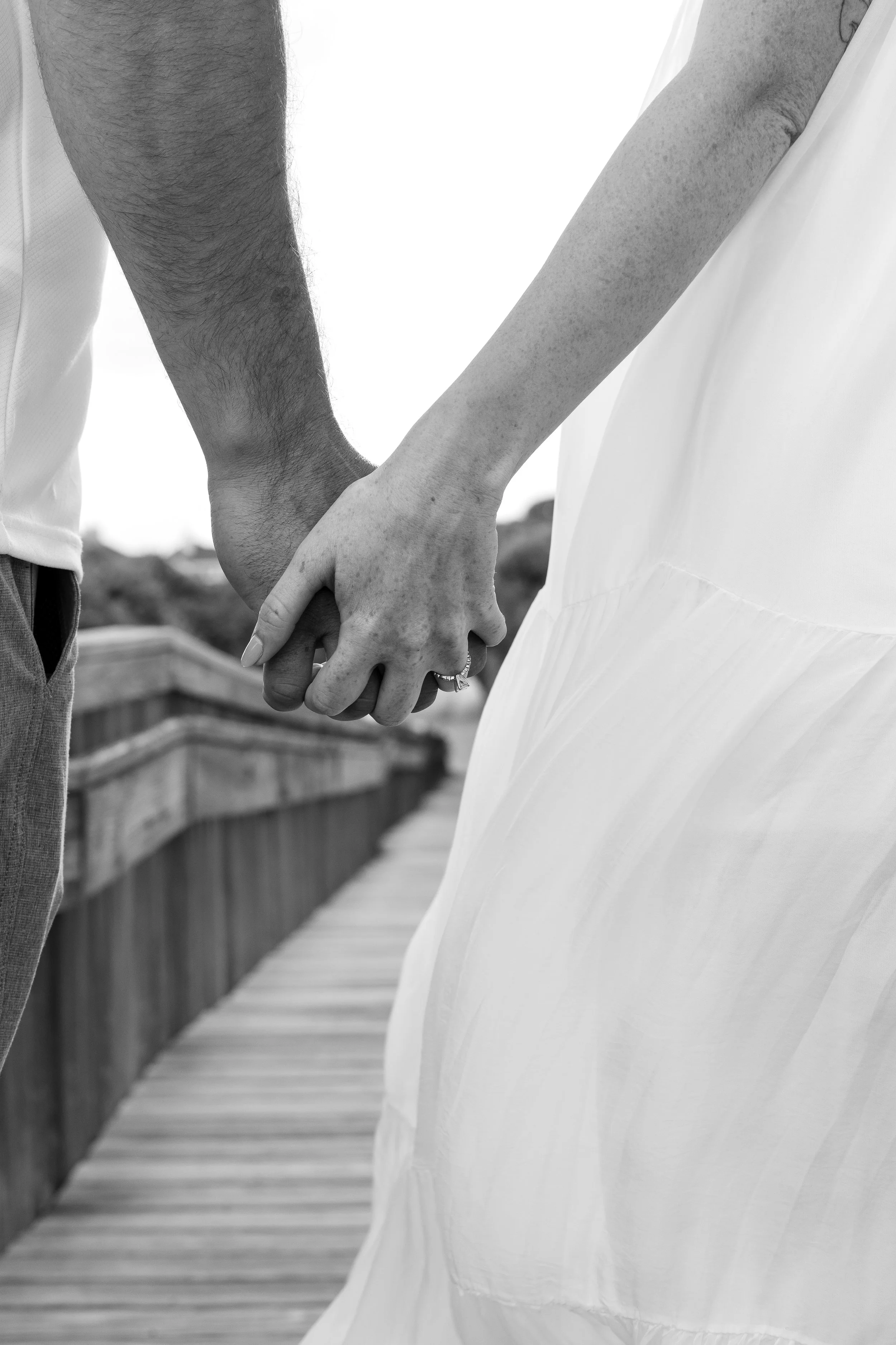 Close-up of a couple holding hands on a wooden bridge outdoors, black and white image.