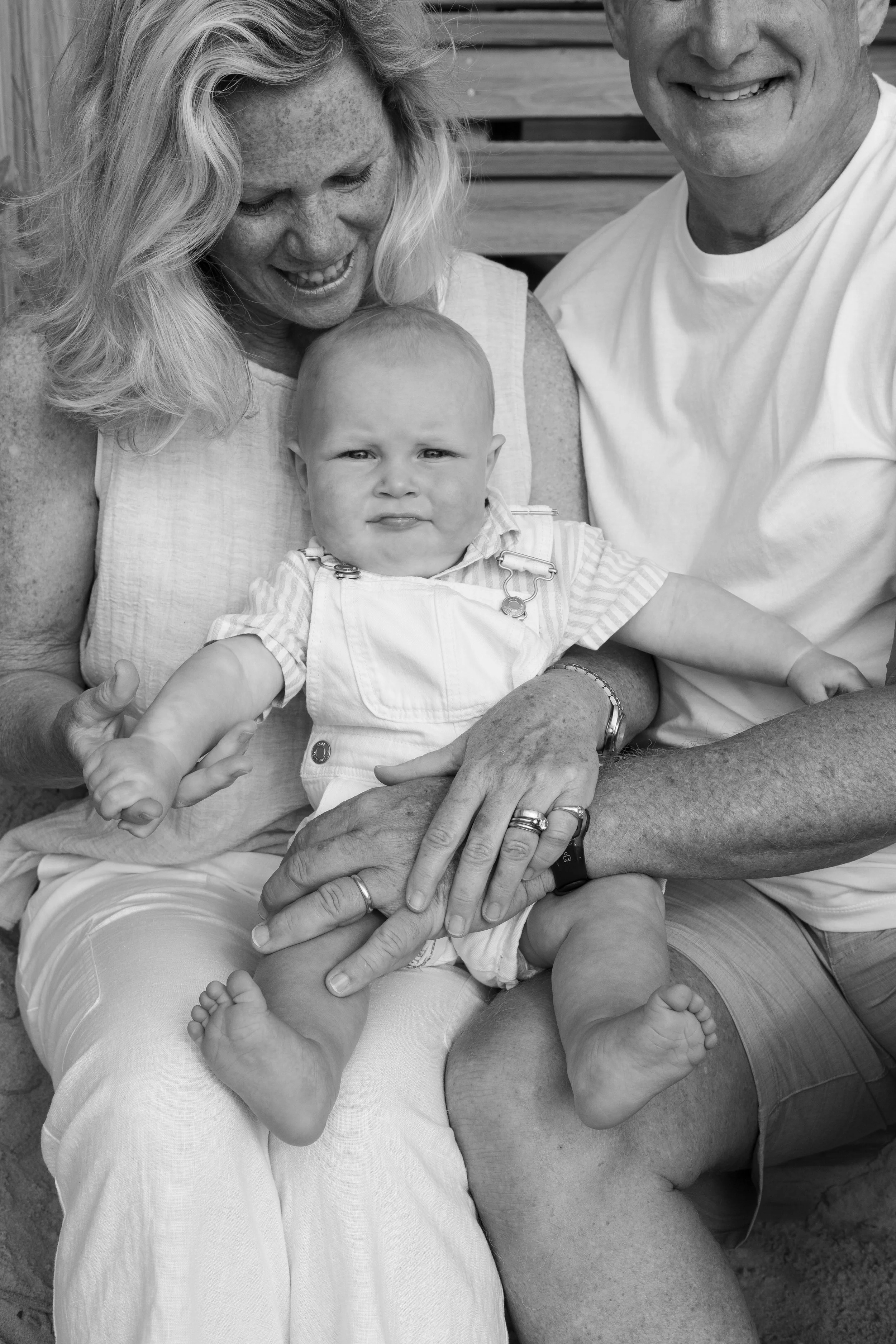 Black and white photo of a toddler with a sour expression sitting on an adult man's lap, surrounded by two smiling women.
