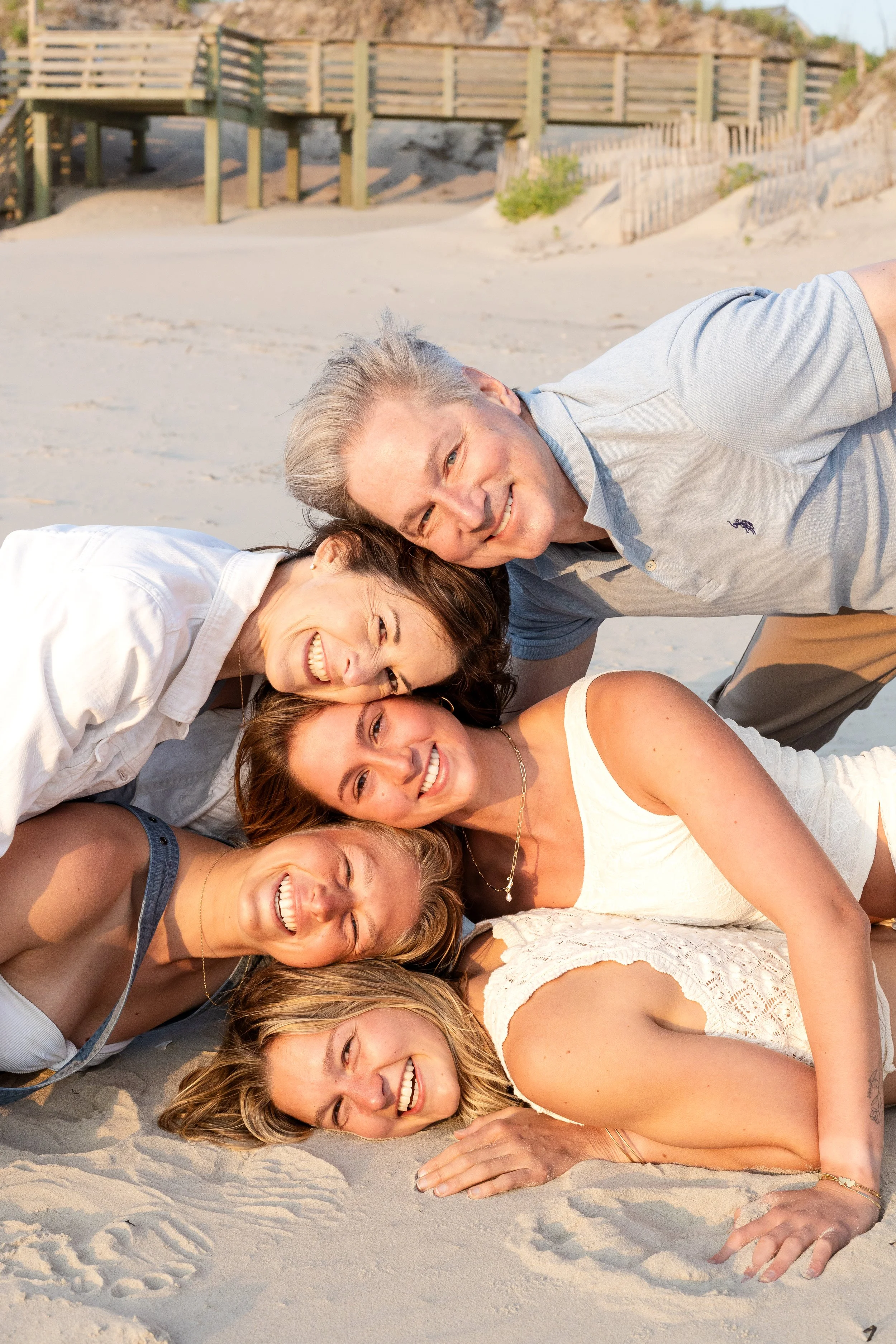 Group of six friends lying on the beach sand, smiling and enjoying a sunny day.