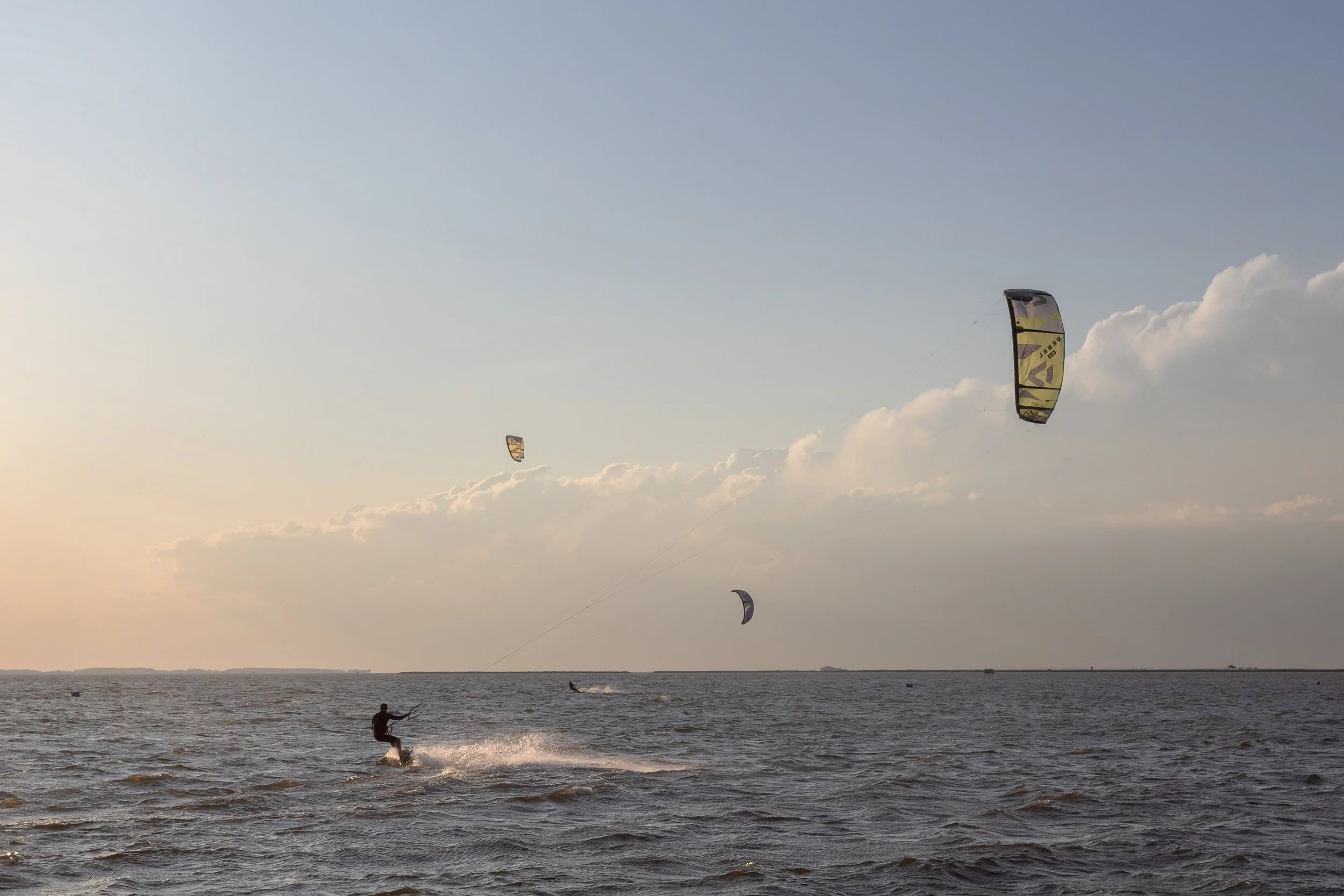 People kite surfing on the ocean during sunset or sunrise with a few scattered clouds in the sky.