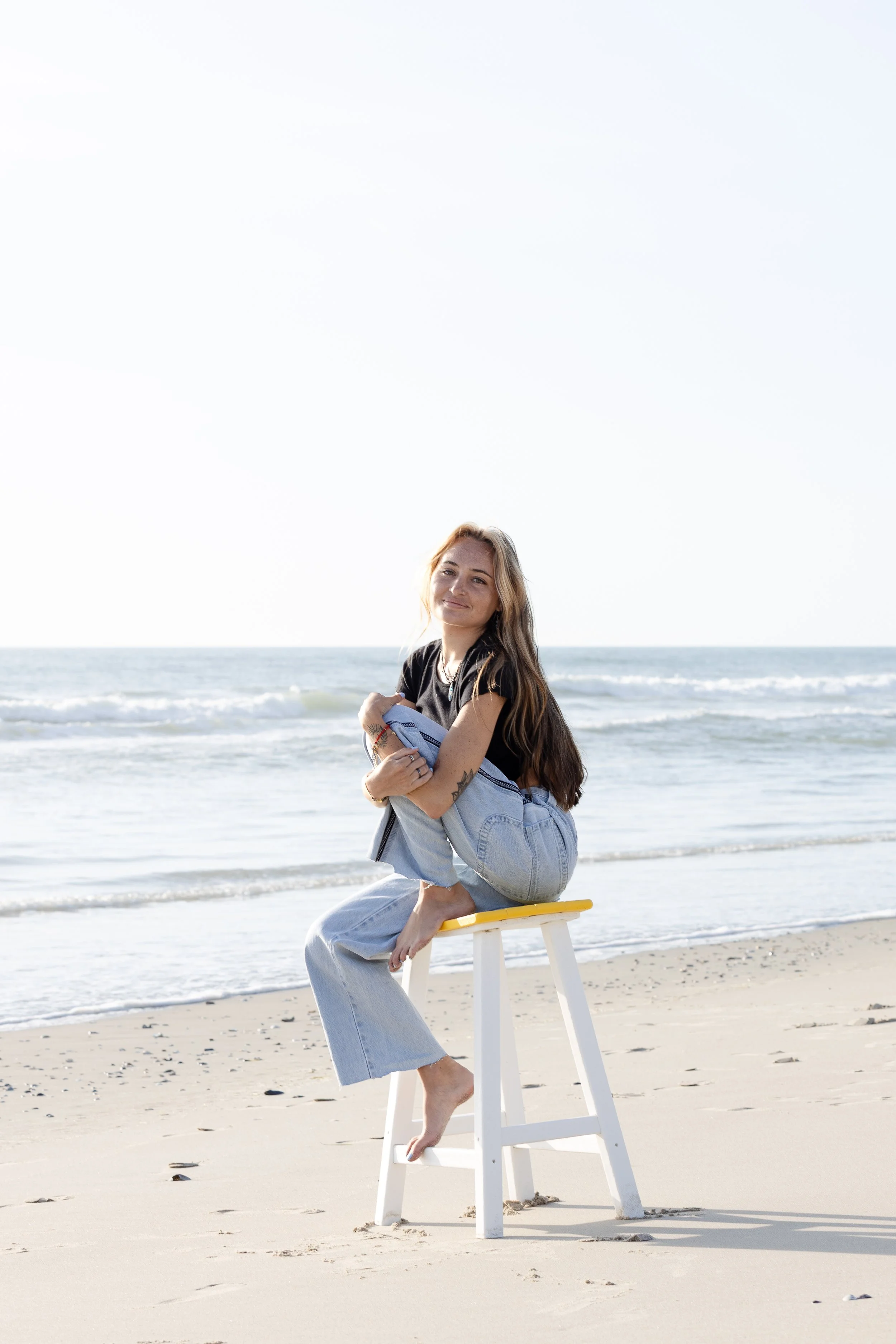 A woman sitting on a yellow stool on the beach with the ocean in the background