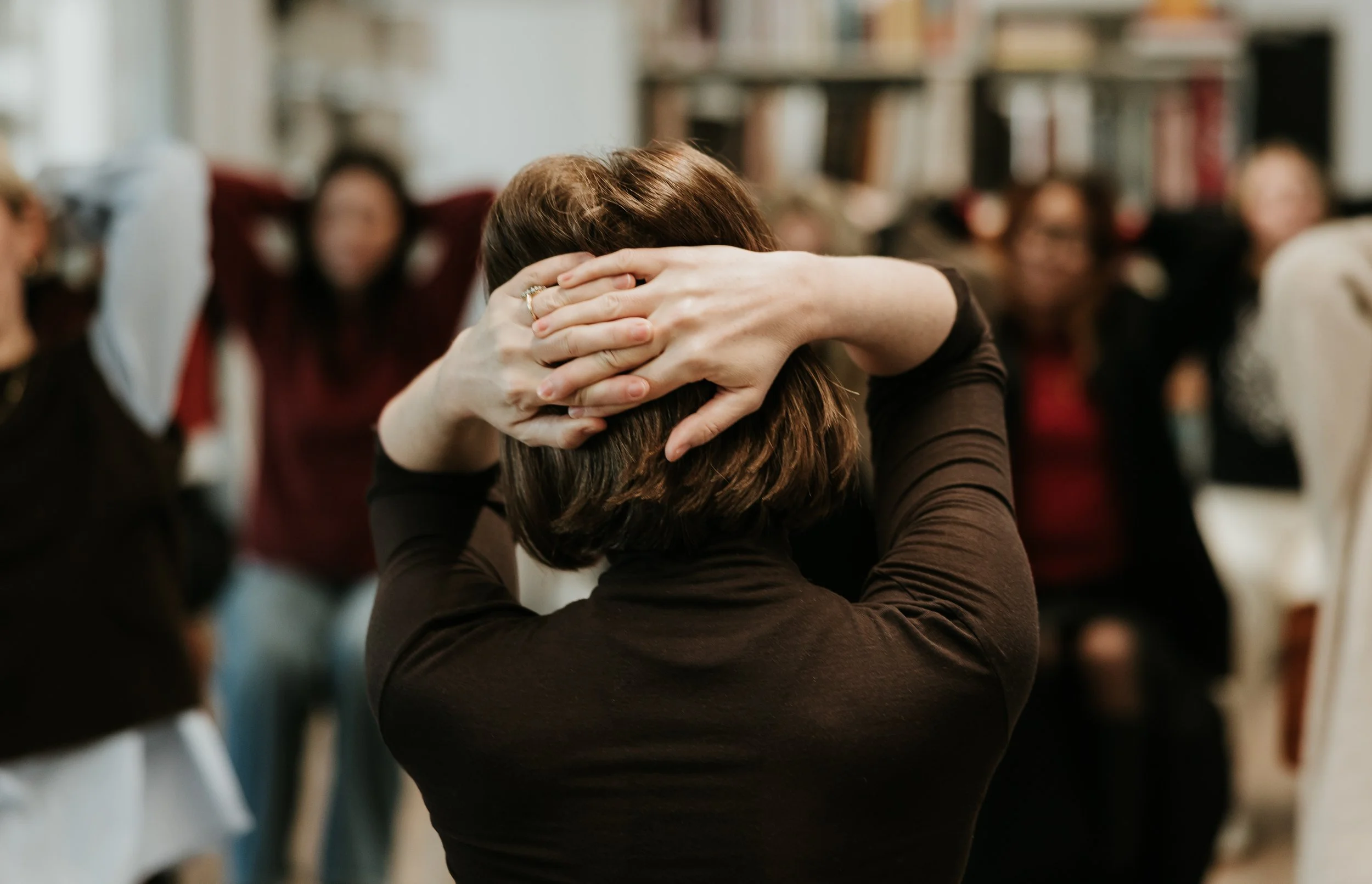 A person sitting with their foot extended and resting on a chair, wearing black sneakers with white stripes, white socks, and black pants. The background shows other people sitting at tables.