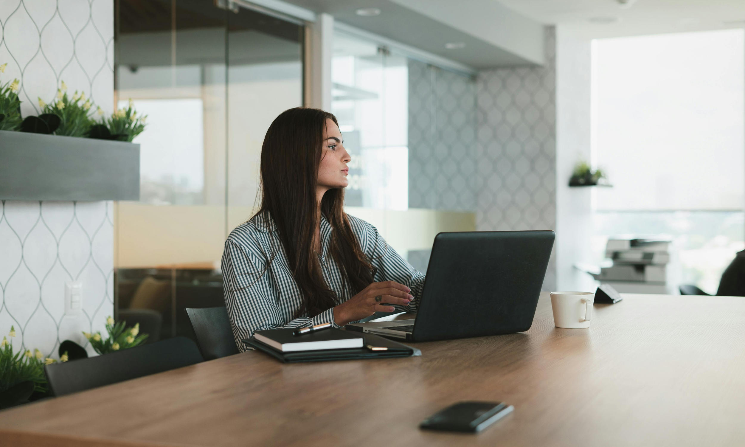 woman sitting at a desk on her laptop, she is looking away from the computer. She is thinking