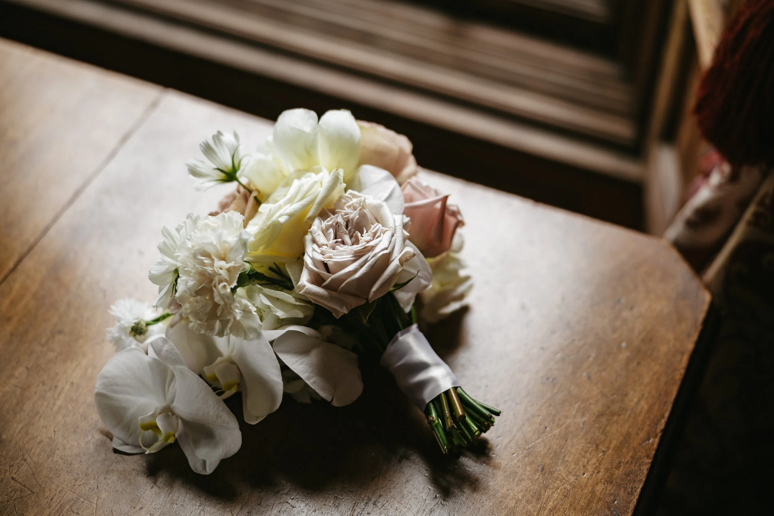 A bouquet of white and pale pink flowers resting on a wooden surface.