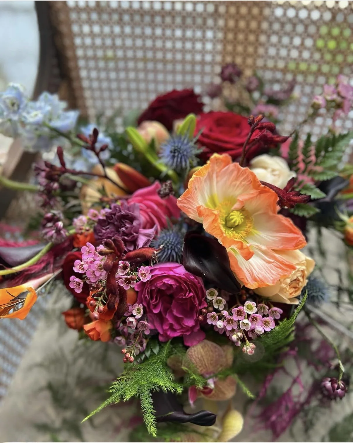 Close-up of a colorful bouquet of assorted flowers, including roses, tulips, poppy, and other blooms, with a woven background.