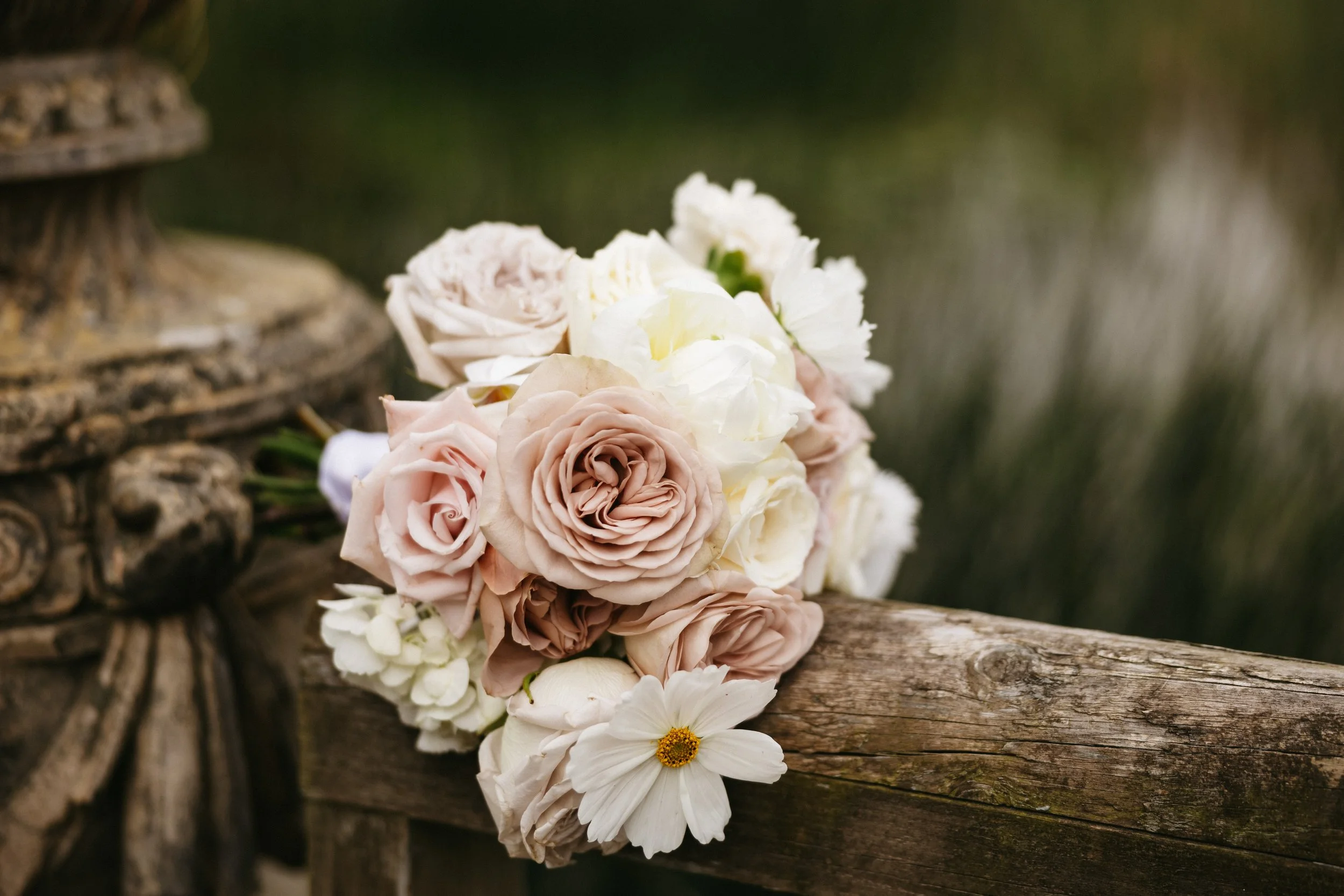 A bouquet of pink and white roses and daisies resting on a weathered wooden railing outdoors.