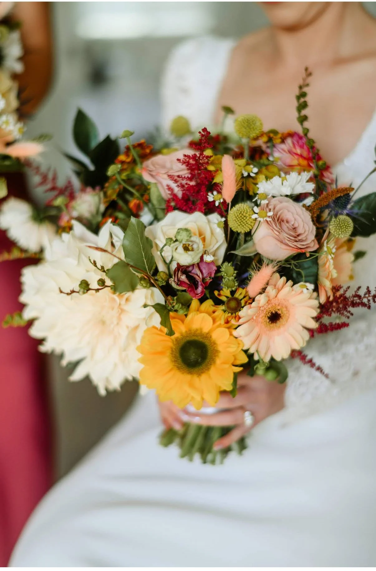A person in a white dress holding an autumnal color bouquet of various flowers including sunflowers, daisies, and roses.