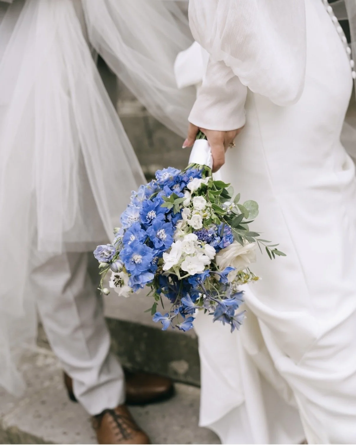 Person in white clothing holding a bouquet of blue and white flowers.