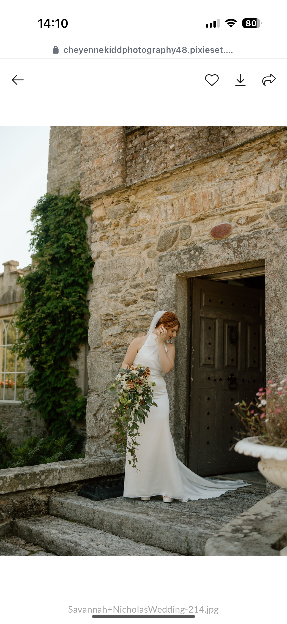 Bride in white wedding dress with veil holding a bouquet of flowers, standing outside a stone building near a black door.
