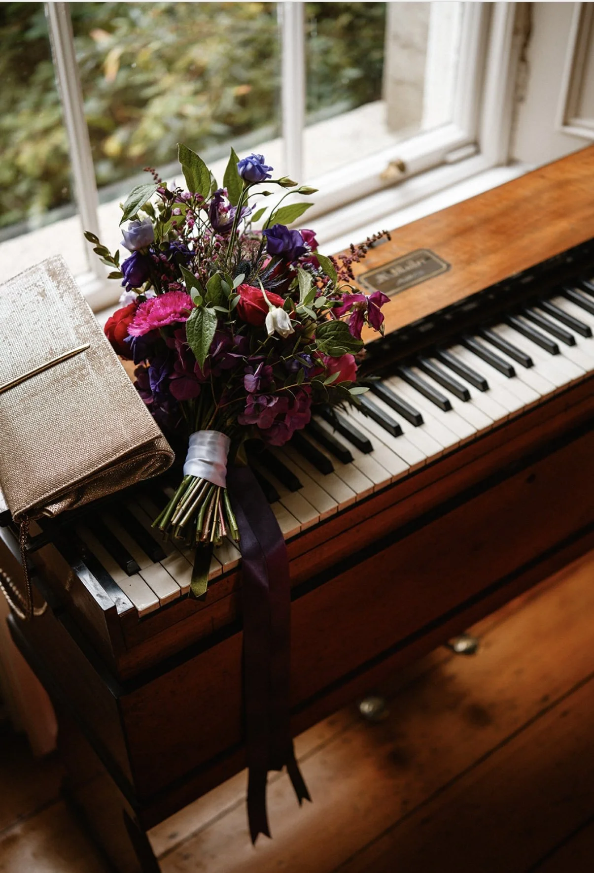 A bouquet of colorful flowers resting on a piano keyboard near a window.