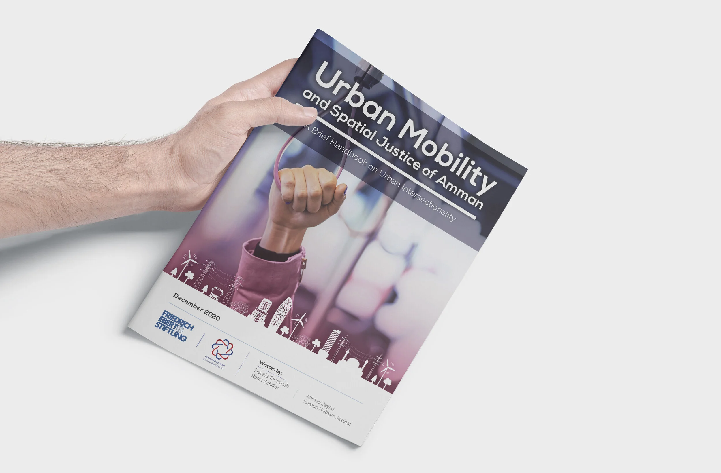 A person holding a magazine titled 'Urban Mobility and Spatial Justice of Amman,' featuring a raised fist clutching pink headphones on the cover, with cityscape and wind turbine illustrations at the bottom.