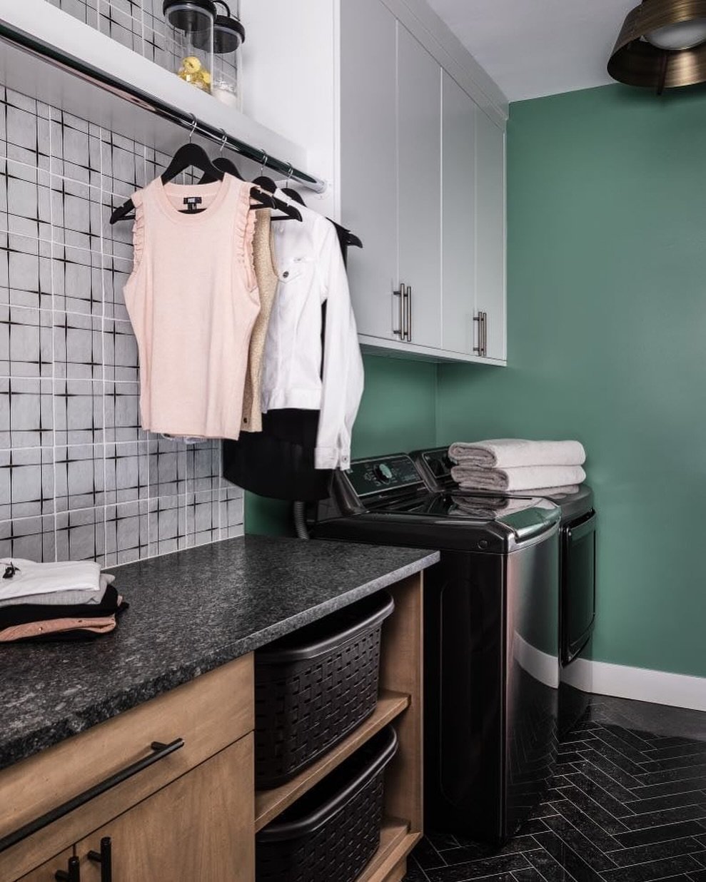 Crisp white upper cabinets and warm wood lowers offer plenty of hidden storage, while the generous countertop makes folding a breeze. A chrome hanging rod &mdash; perfect for air-drying or staging outfits &mdash; spans the modern, grid-patterned wall