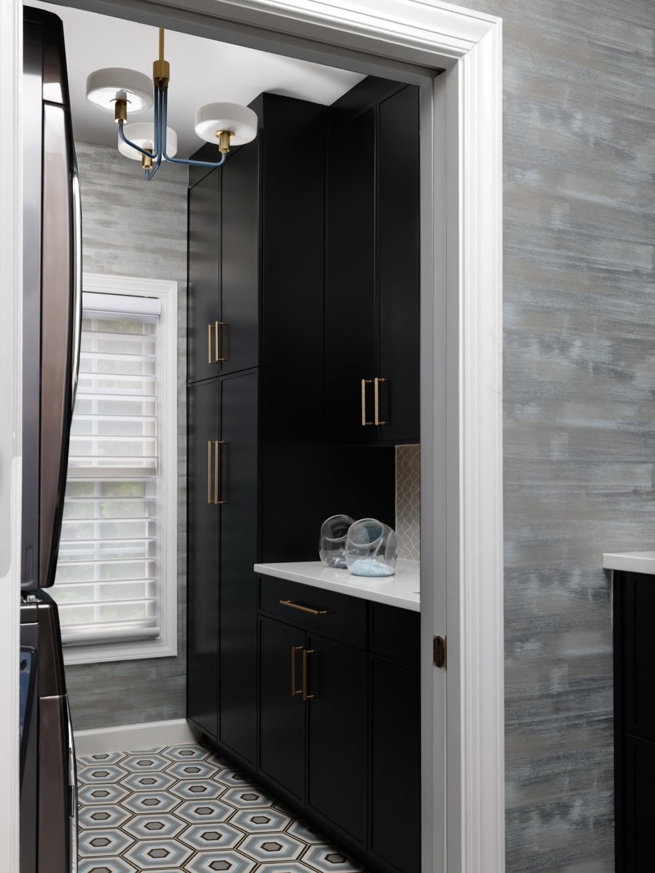 This mudroom&ndash;laundry combination was designed to work hard while still feeling polished. 

Custom cabinetry keeps everyday items tucked away, while the dark finishes add depth and contrast against the textured walls and patterned floor.

It&rsq