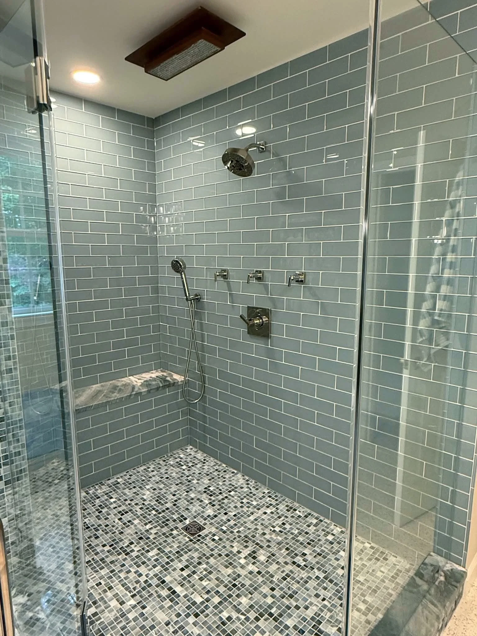 The rain showerhead in this Bethesda bathroom has a cool feature &mdash; it lights up when the water turns on, adding an unexpected glow overhead. ✨

We paired it with soft blue-green tile, a mosaic floor, and natural stone accents to create a shower