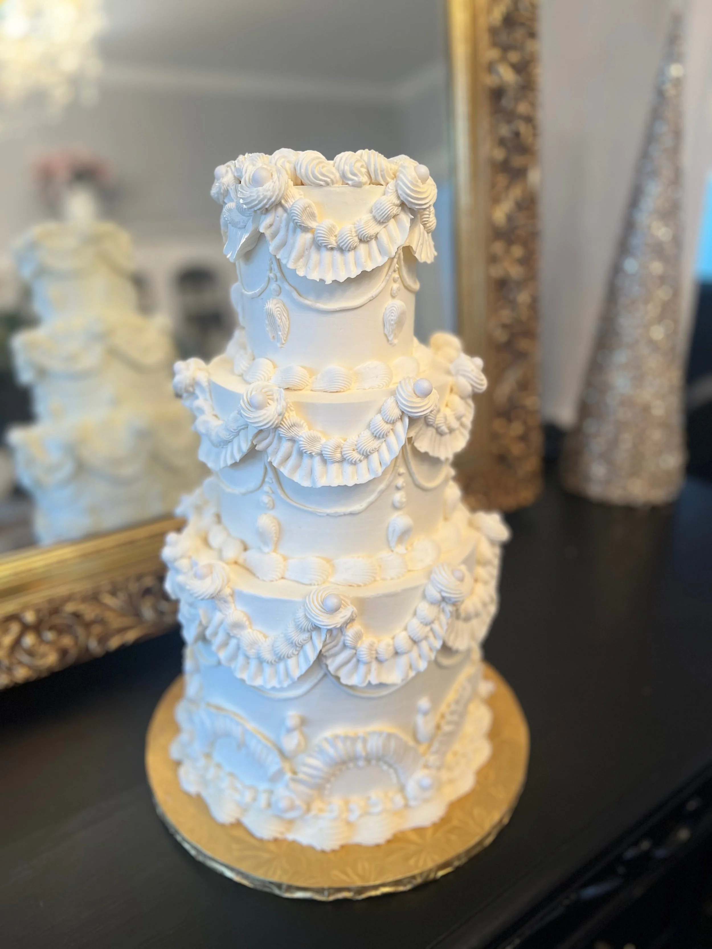 Three-tiered white wedding cake decorated with piped frosting garlands and rosettes, on a gold cake board.