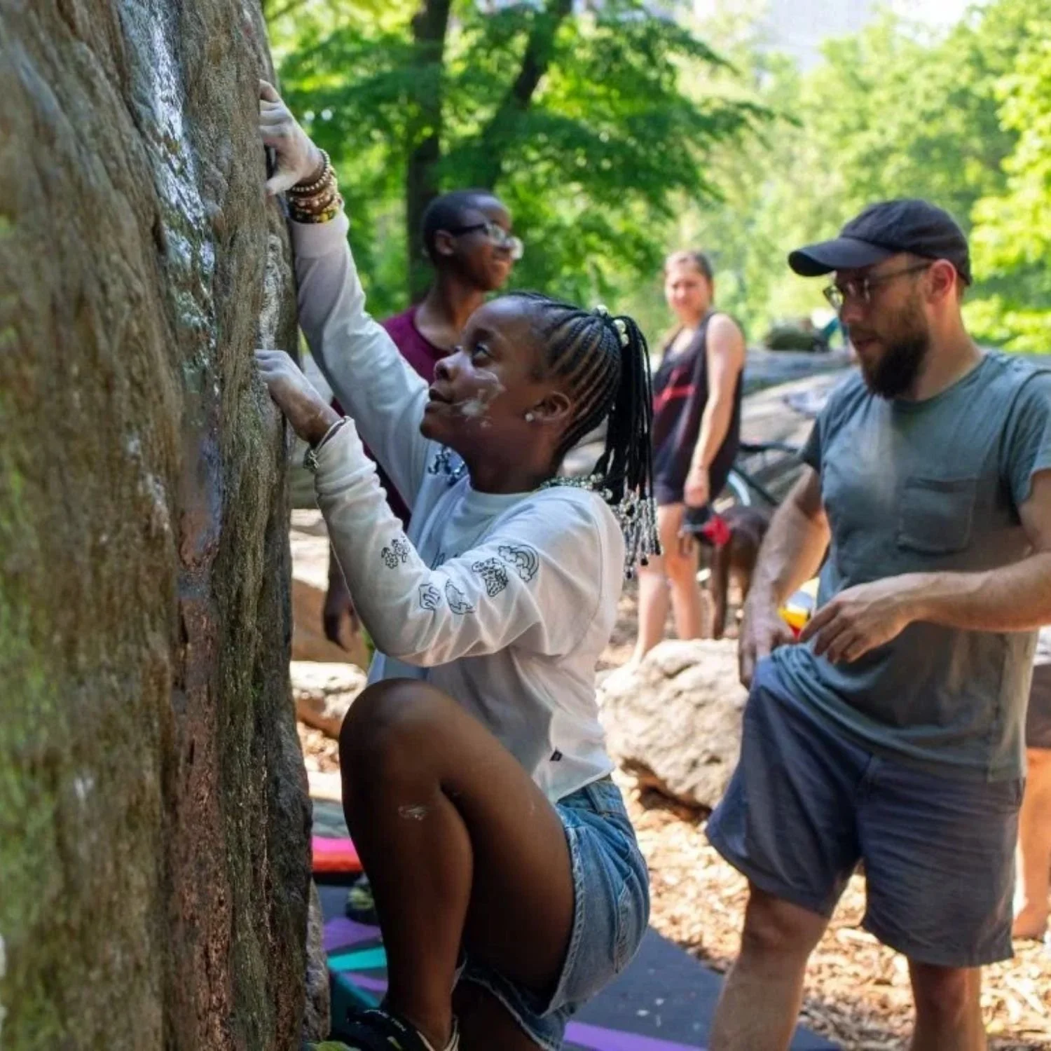 A young girl focusing while climbing a natural rock boulder outdoors.