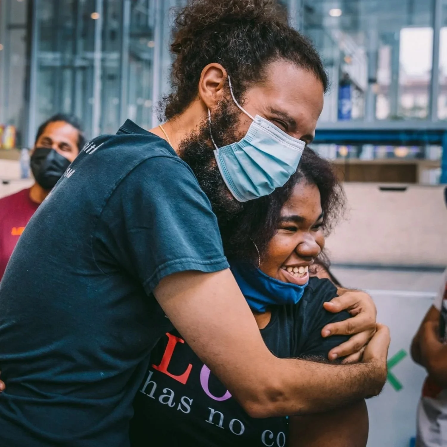 A mentor and student laughing and hugging at an indoor climbing facility.
