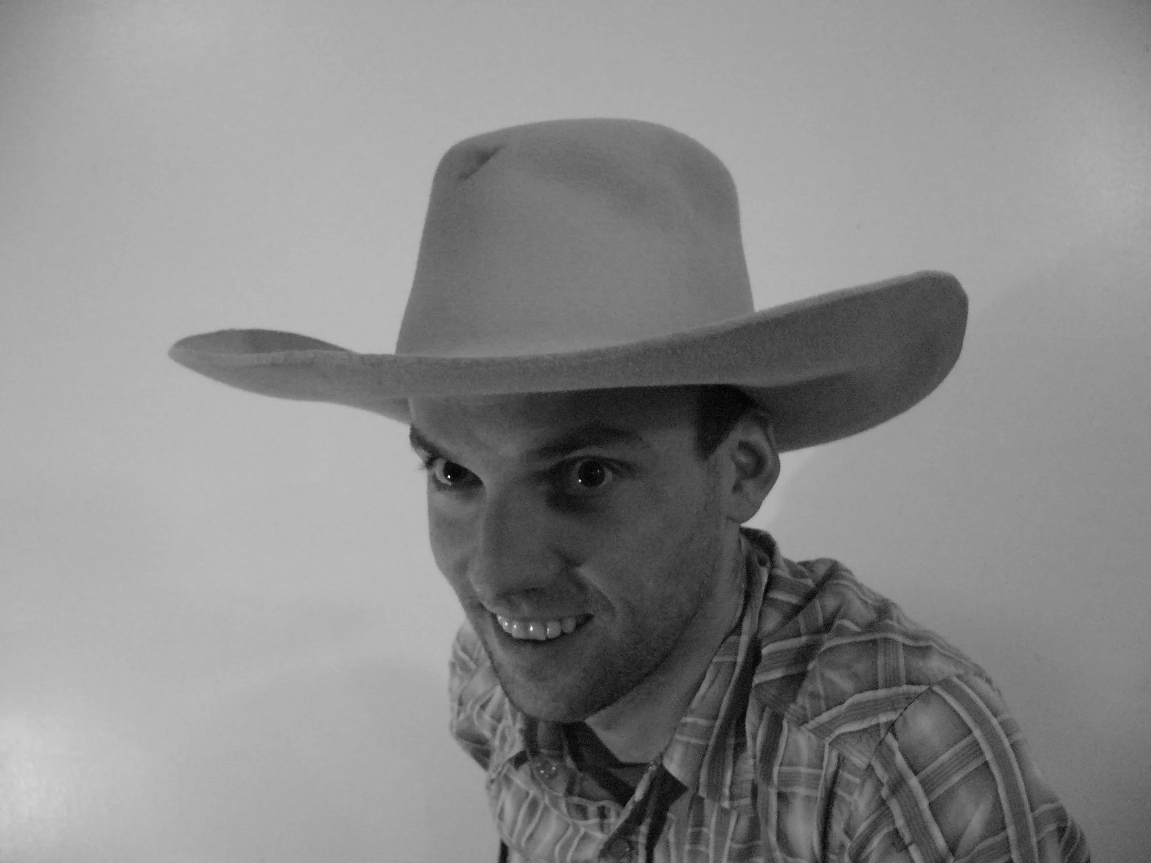 A man wearing a cowboy hat and a plaid shirt, smiling, in black and white.