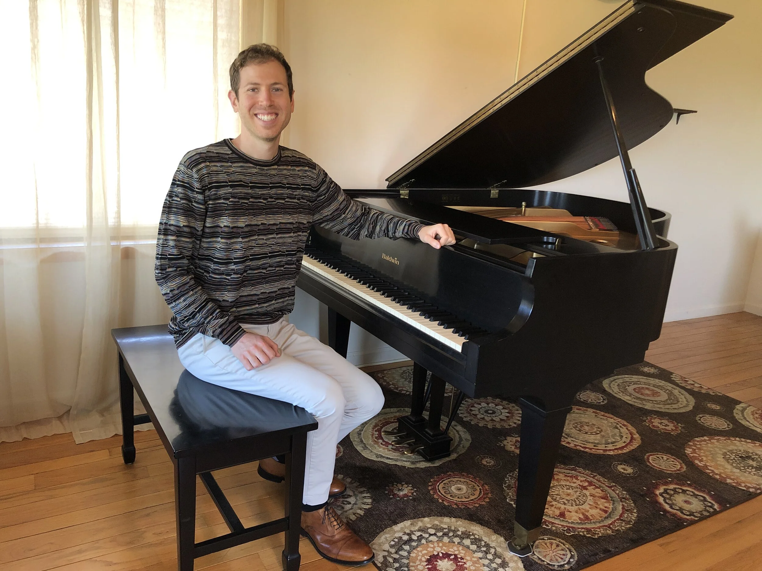 Josh Benson-Merron, piano teacher, seated beside a grand piano