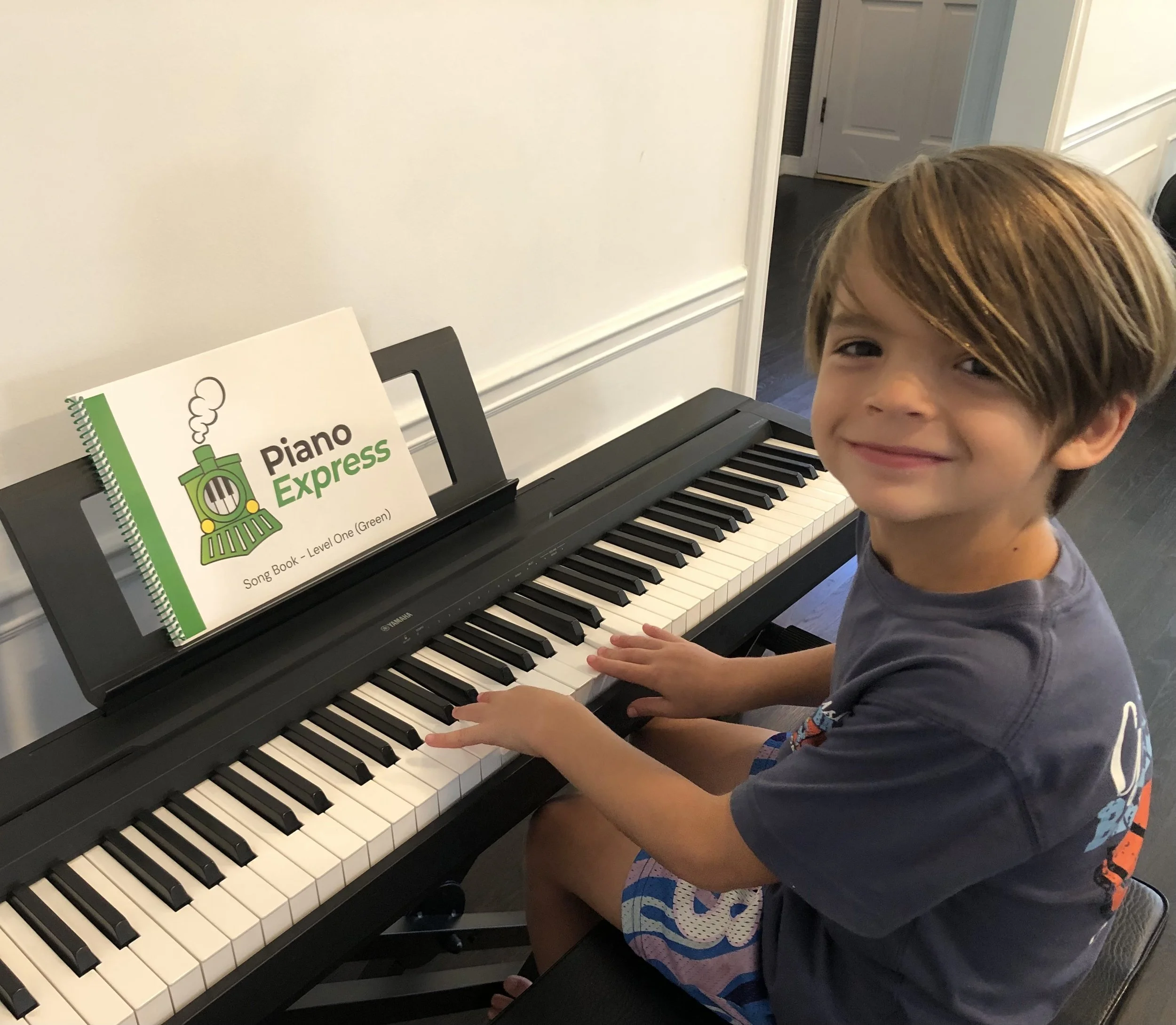 Piano student smiling at the keyboard with a Piano Express song book